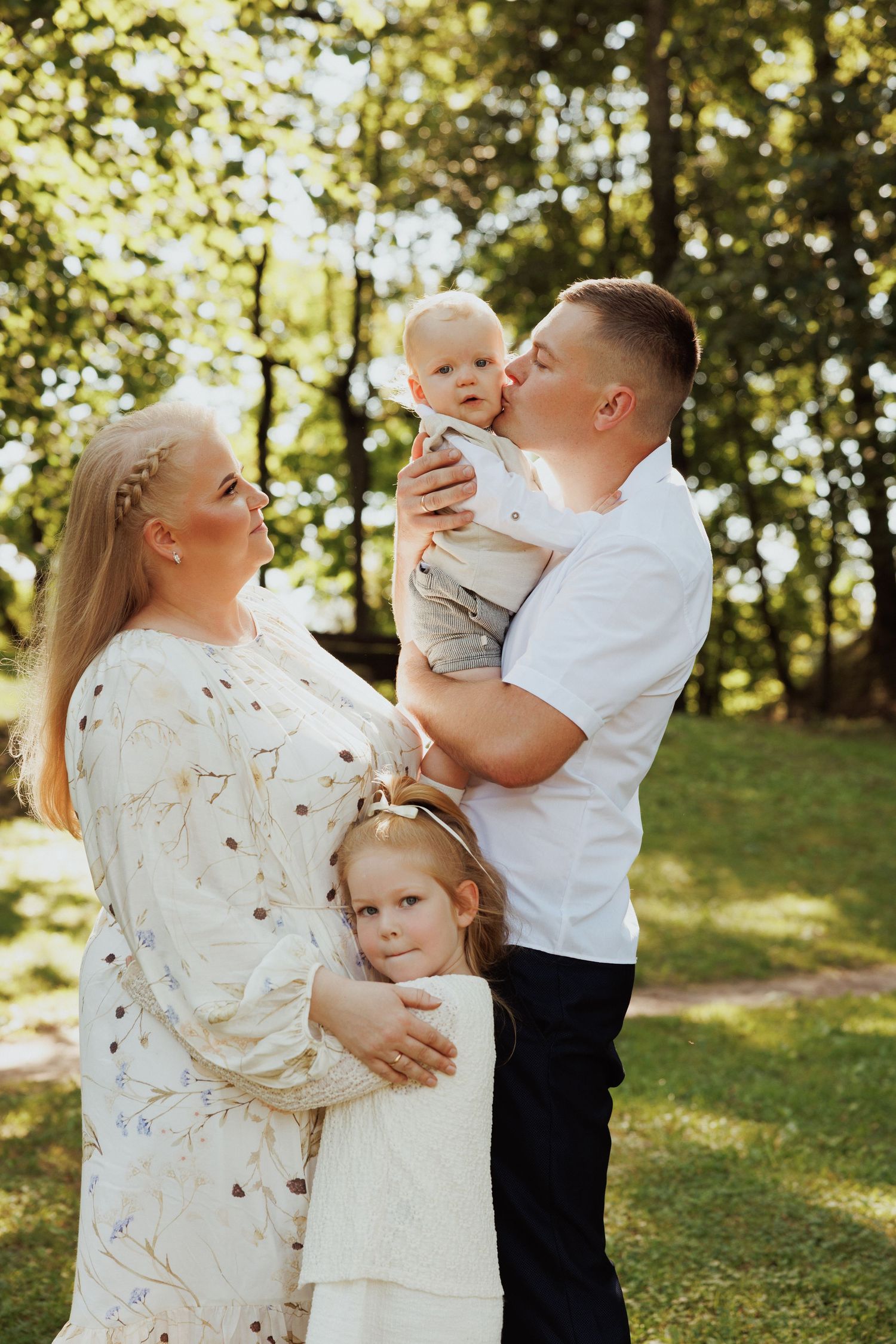 Family portrait in a sunlit forest setting wearing coordinated white and cream outfits.