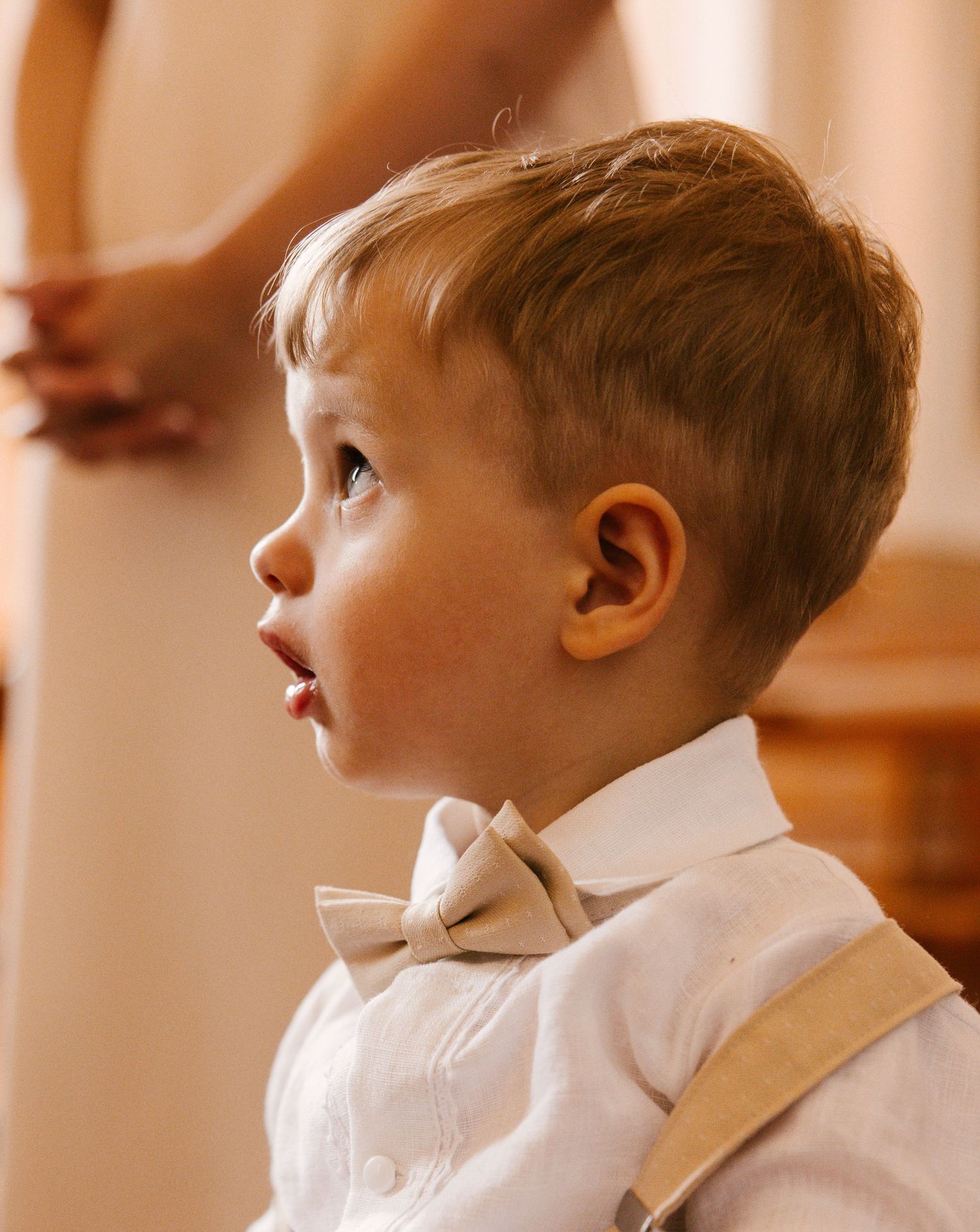 A young boy in a white dress shirt looks to the side with a thoughtful expression in a warm-toned setting.