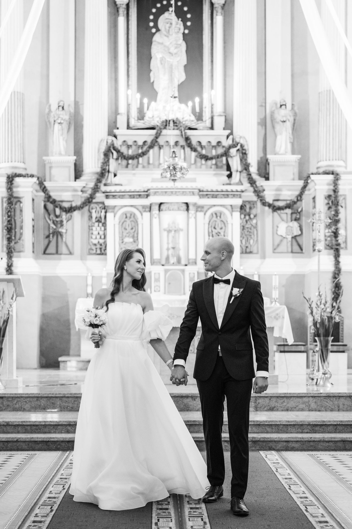 Black and white photo of a wedding ceremony in a grand cathedral with ornate altar and decorative details.