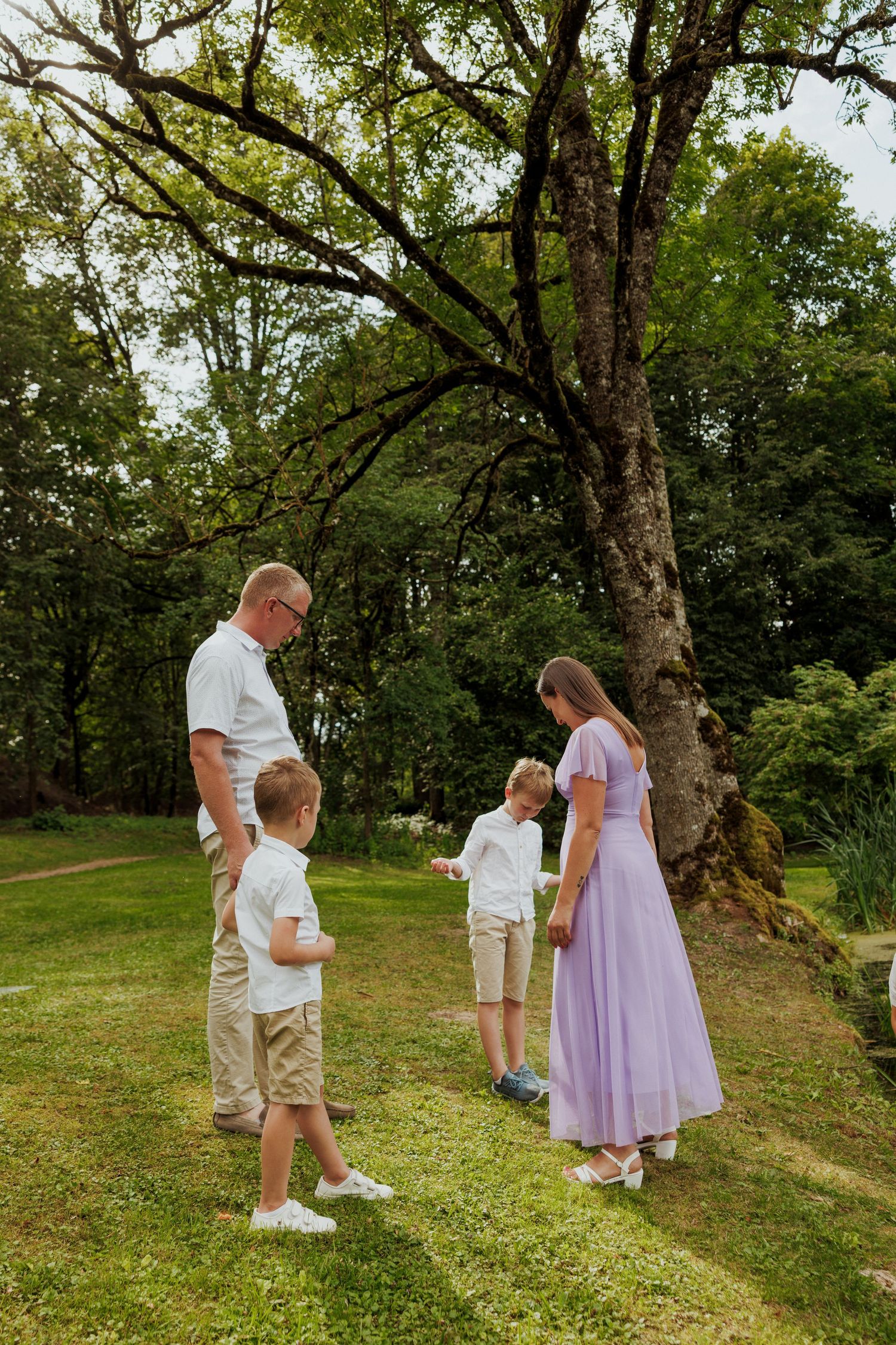 A group gathers under a large tree on a grassy hill during a sunny summer day in casual attire.