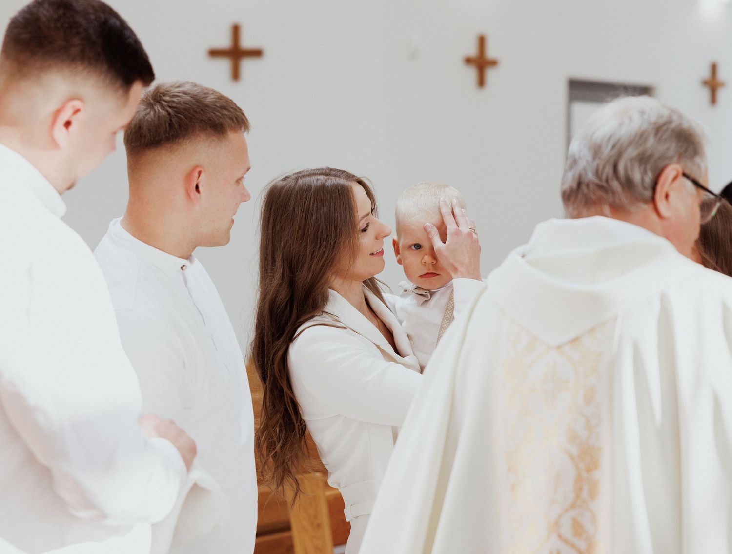 Wedding ceremony attendees in white attire gather at a church with crosses visible on the walls.