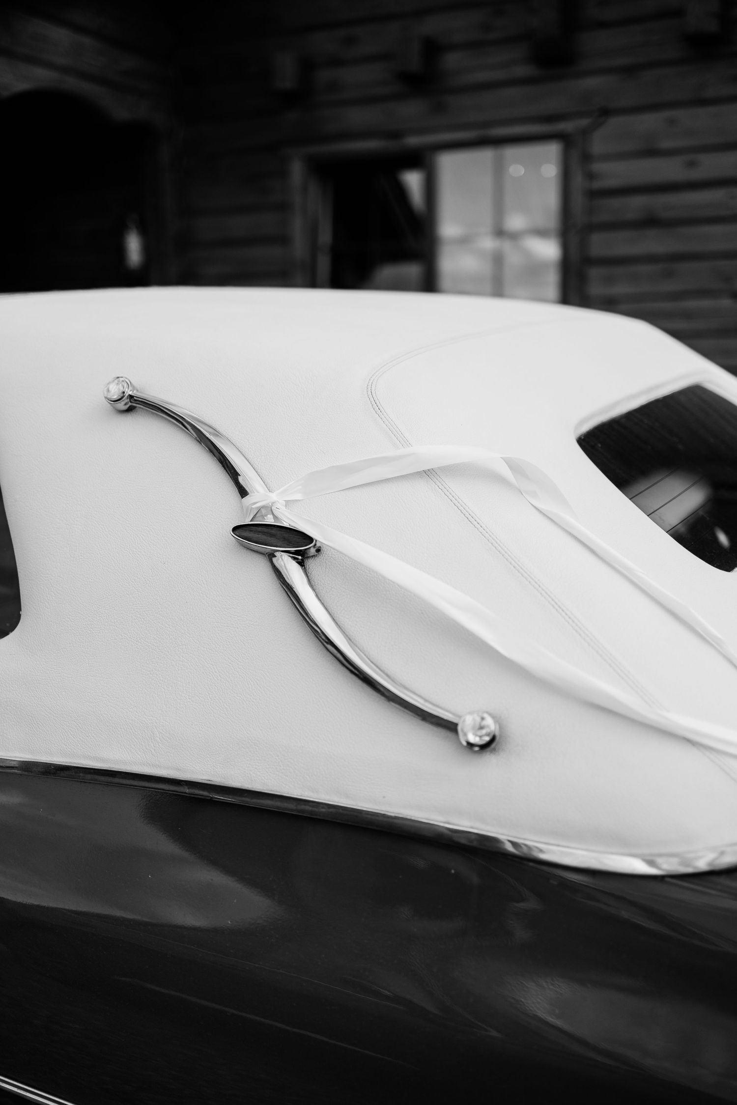Close-up black and white detail shot of a vintage car's curved body lines and chrome trim.