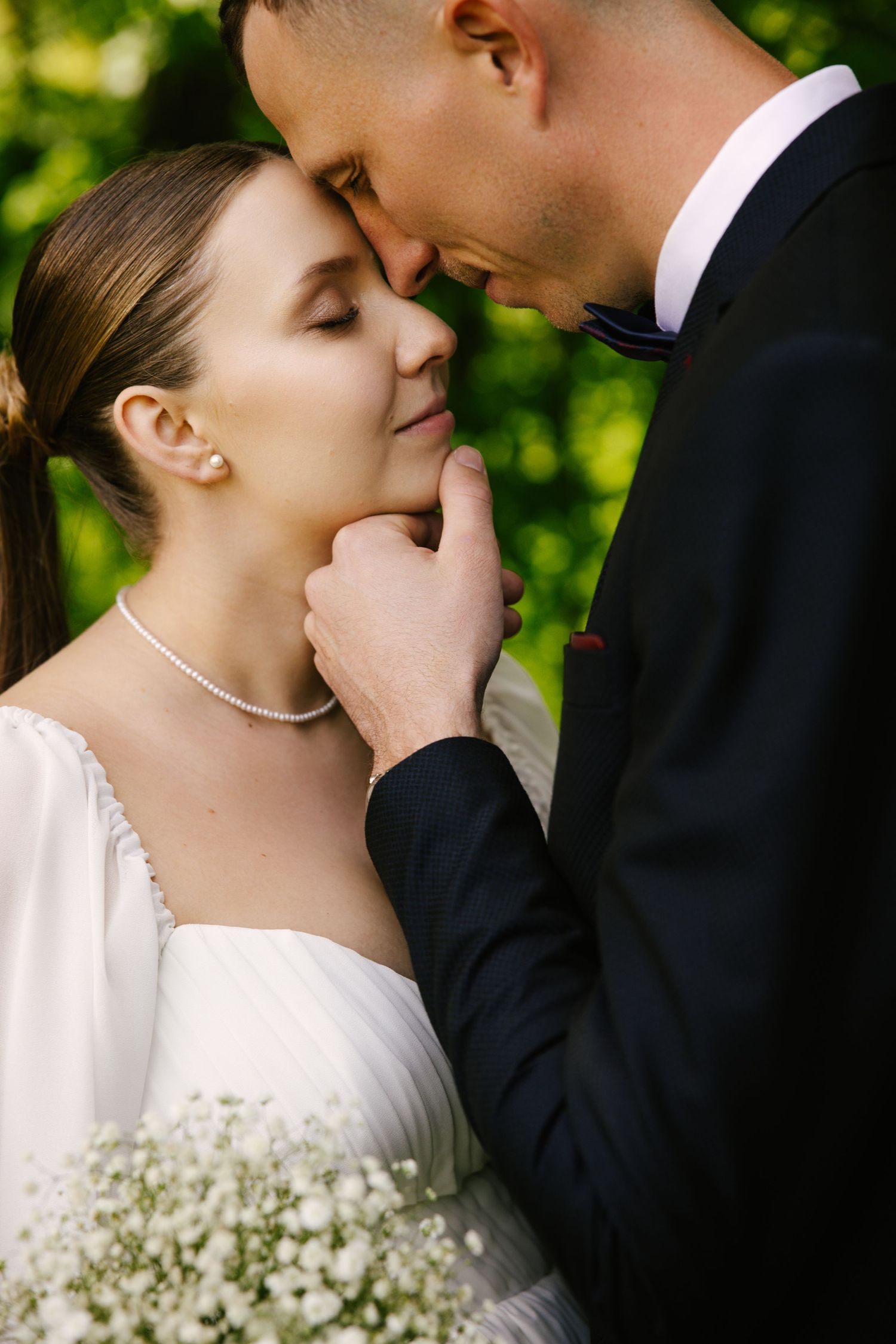 A romantic close-up moment between newlyweds with baby's breath bouquet in a garden setting.