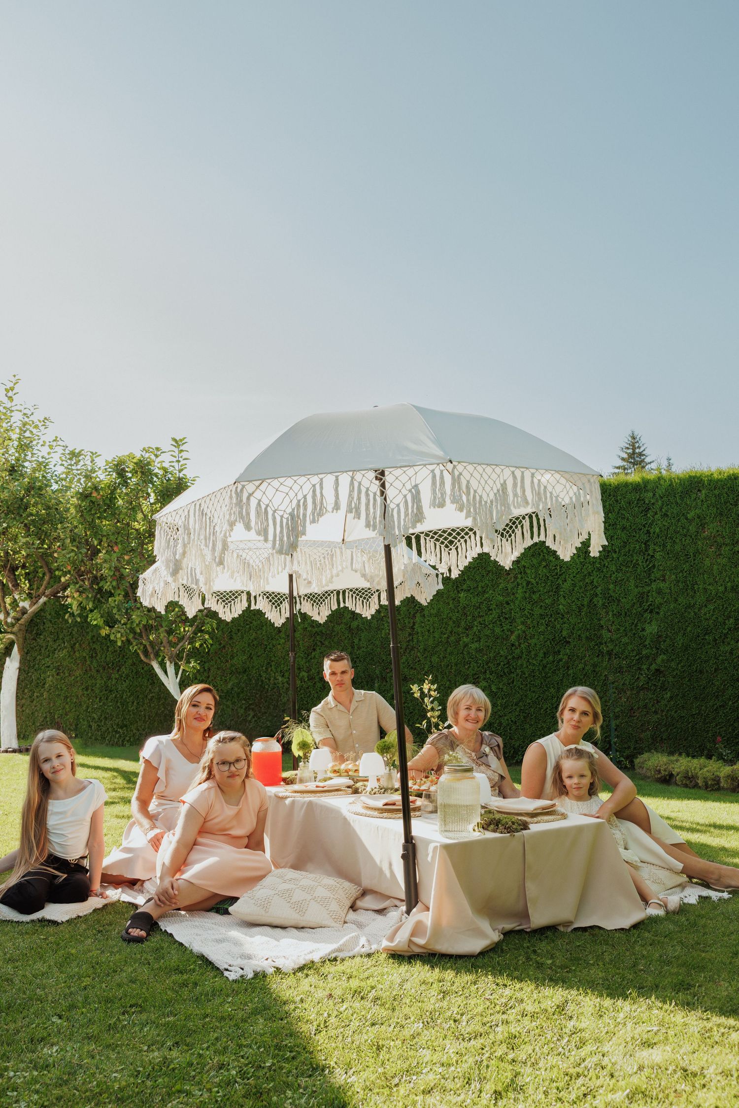 A garden party setup with an elegant white umbrella and people enjoying a picnic on the lawn.