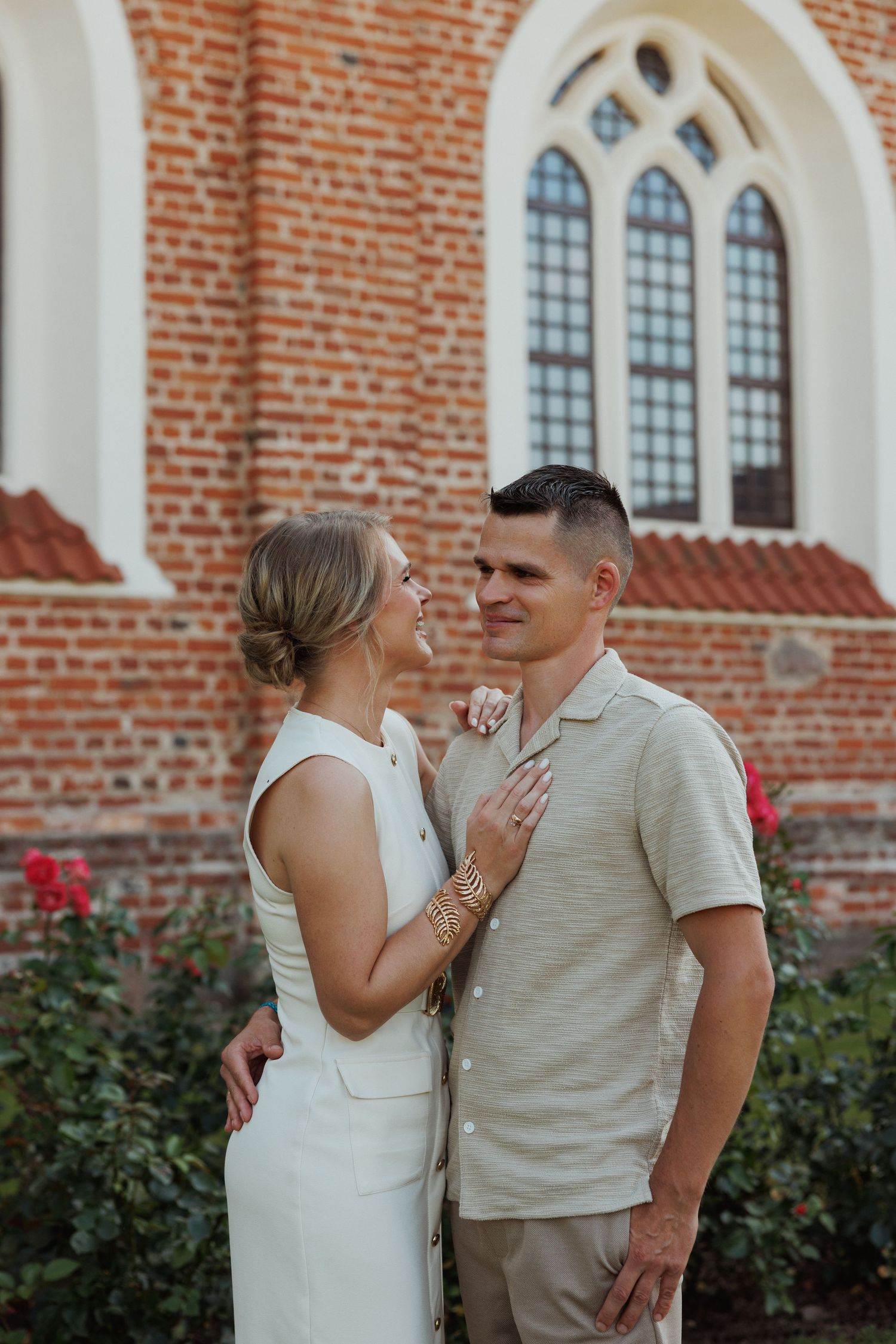 A romantic moment between a couple in front of a brick church with gothic windows.