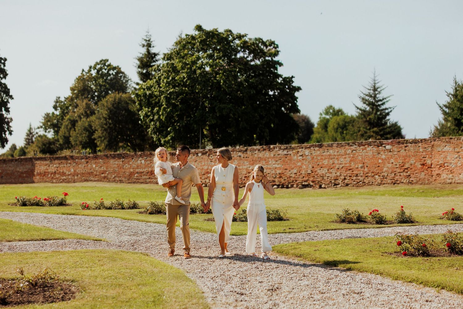 Distant view of people walking along a winding path through a sunny garden landscape.