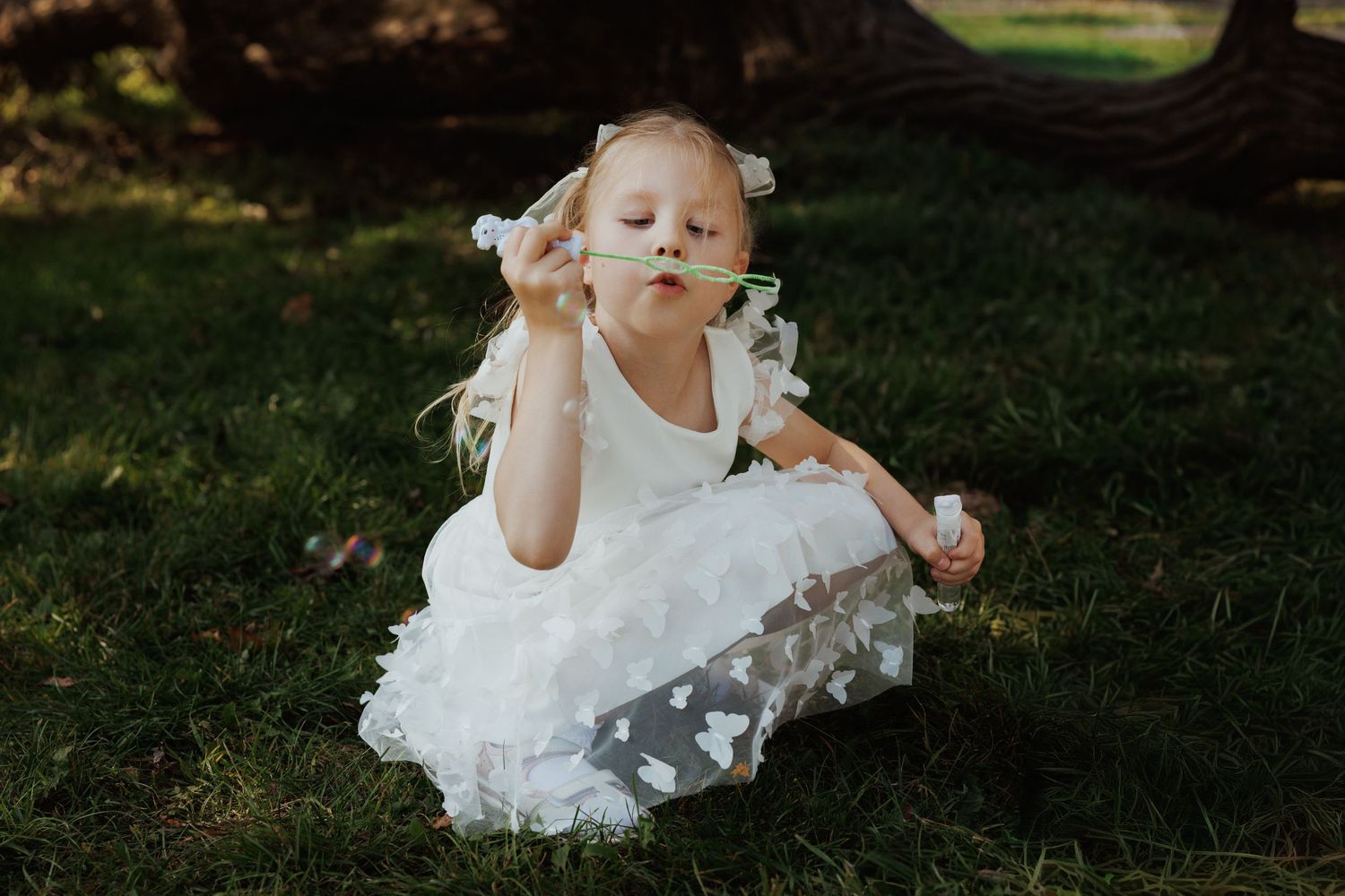 A person in a white lace dress sits gracefully on lush green grass during an outdoor photo session.