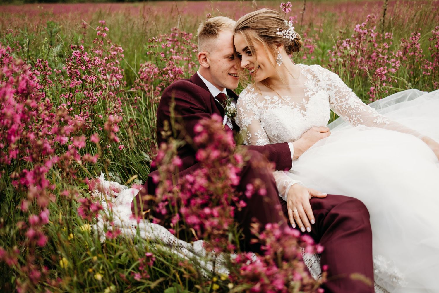 A tender wedding moment captured among pink wildflowers in a meadow.