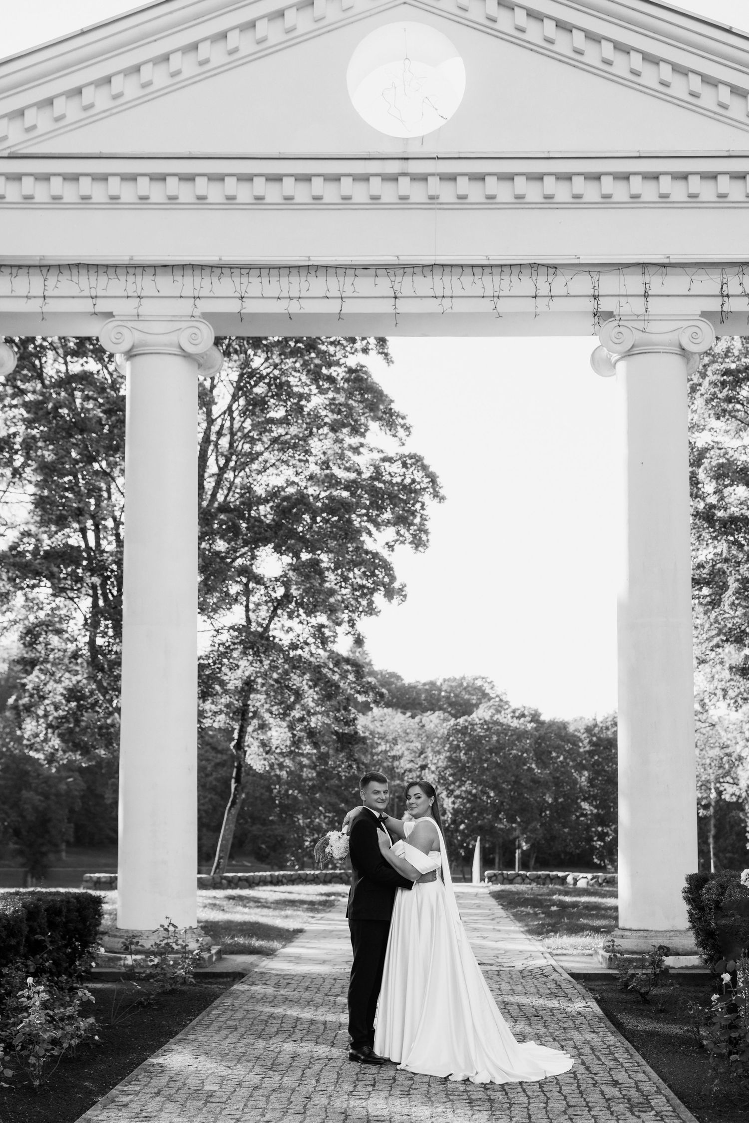 Classic white columned pavilion serves as backdrop for wedding photographs.