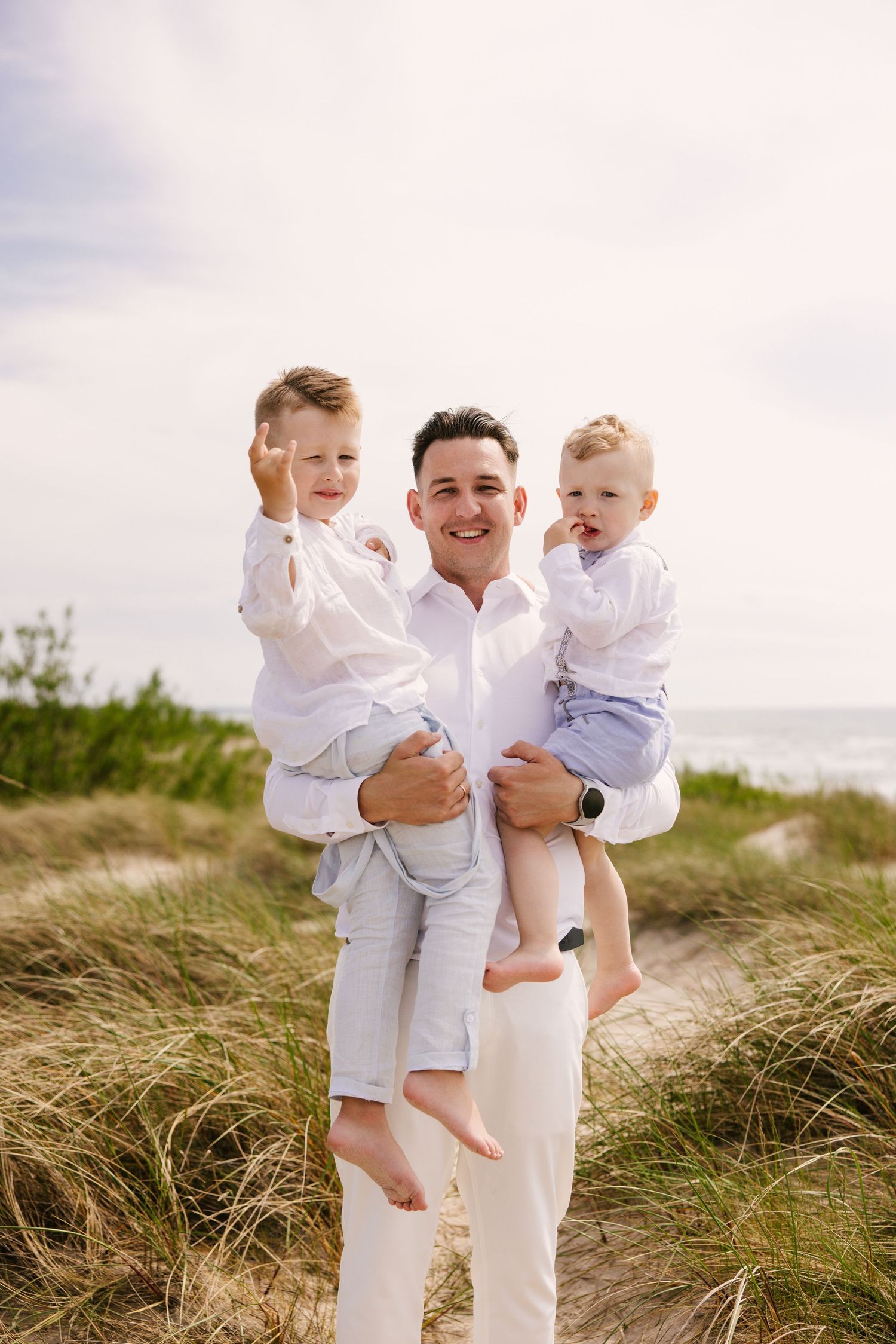 Family dressed in white playing and laughing together on grassy sand dunes by the ocean.