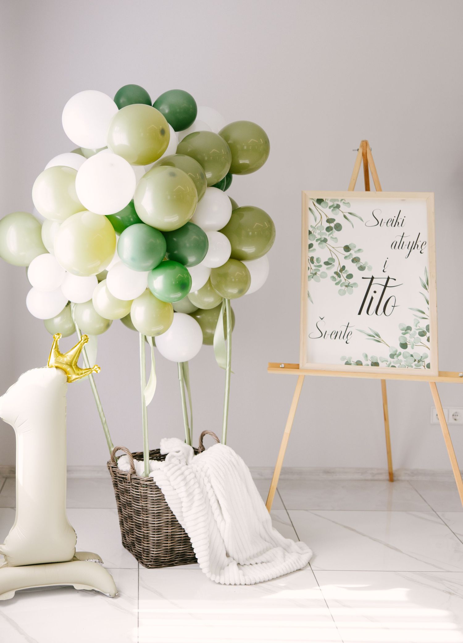 Elegant party decor featuring green and white balloons with wooden easels displaying event signage.