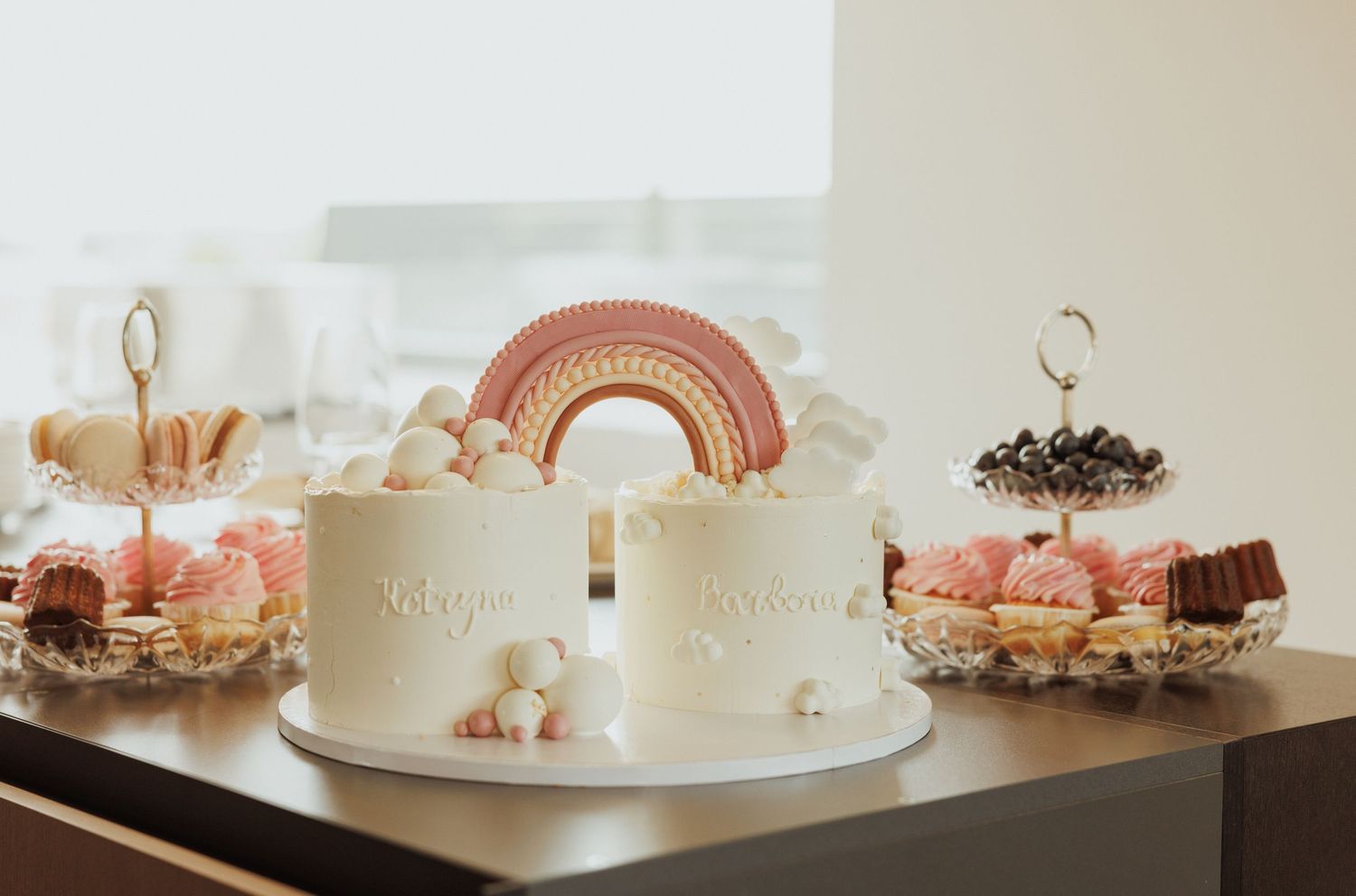 Dessert display featuring pink and white cakes with decorative elements on elegant cake stands.