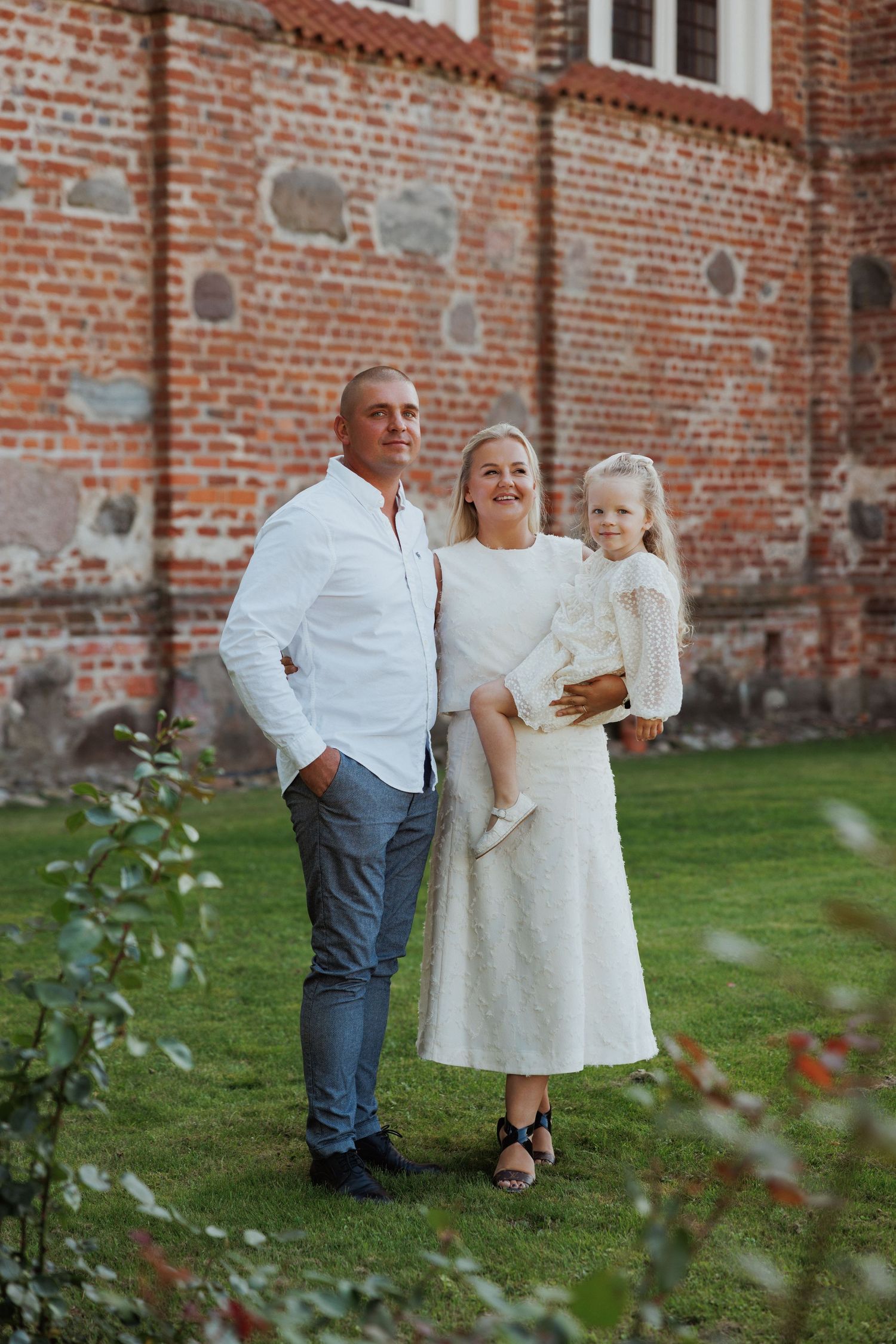 Children in white outfits playing on grass near a rustic brick church wall.