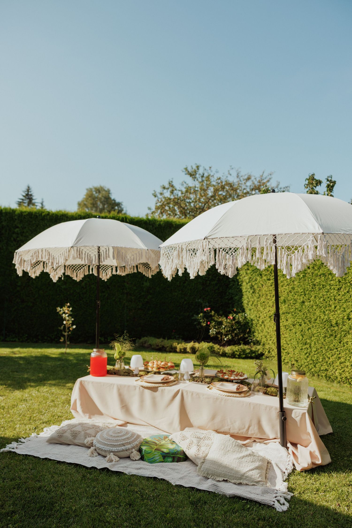 Elegant picnic setup with white fringed umbrellas and table settings on a sunny lawn.