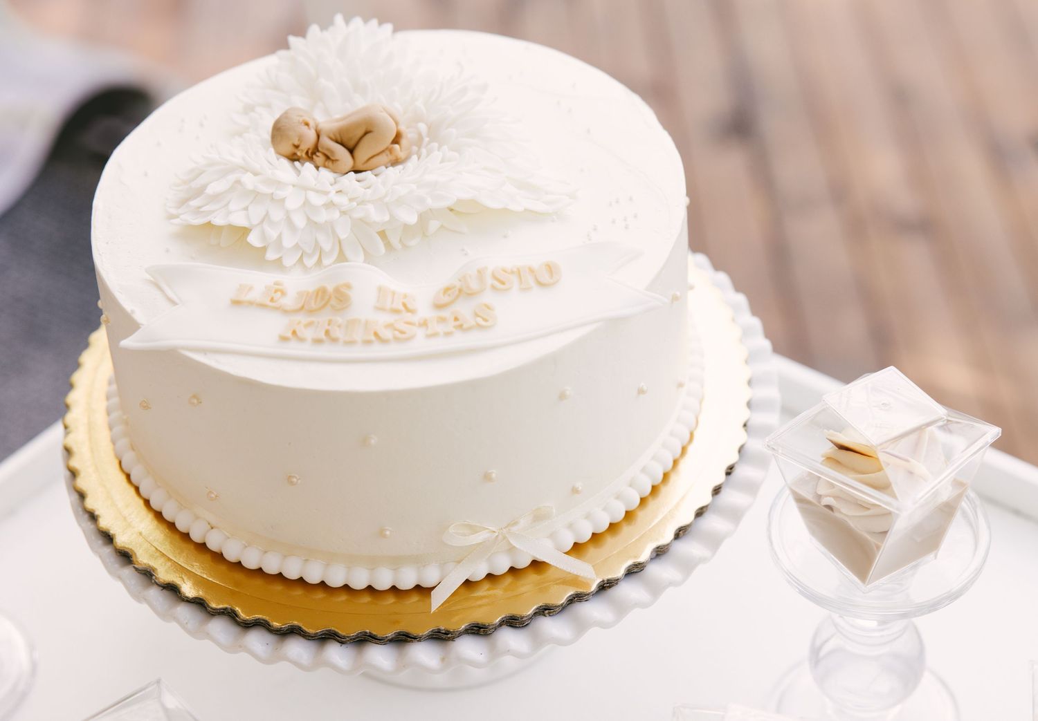 Elegant white wedding cake with delicate floral decoration and gold accents on a wooden surface.