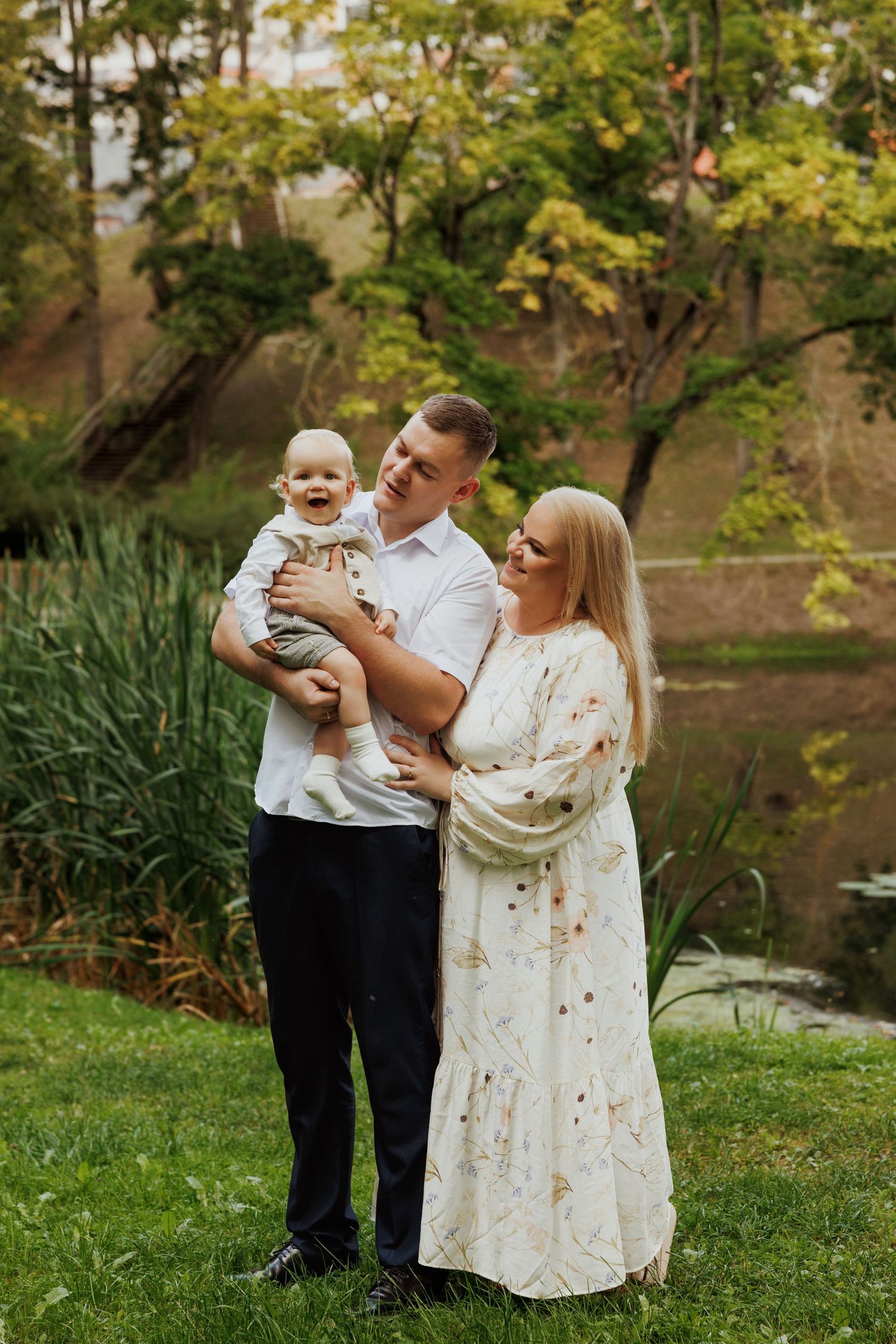 Family poses together in a lush garden setting with pond and trees in background.