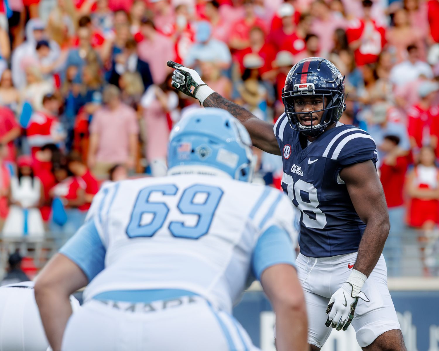 College football player in navy uniform points at opponent in white jersey number 69 during a game.
