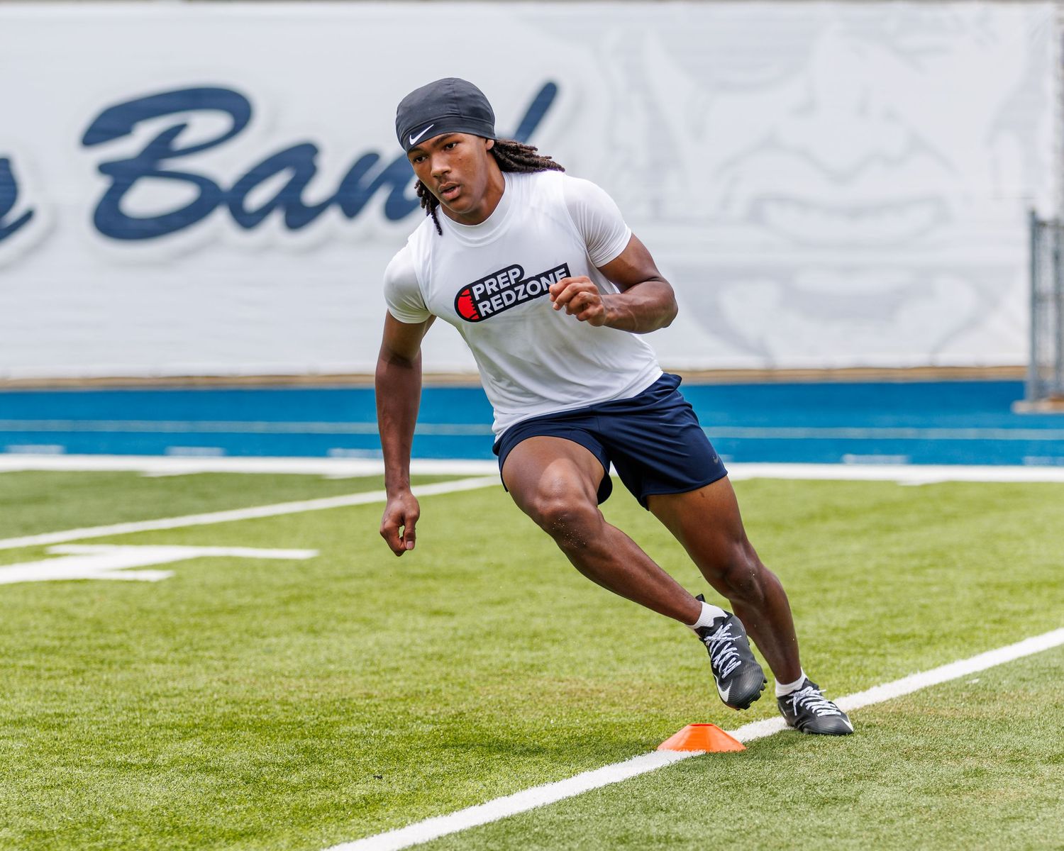 Athlete in white shirt and dark shorts performs agility drill with cones on a football field.