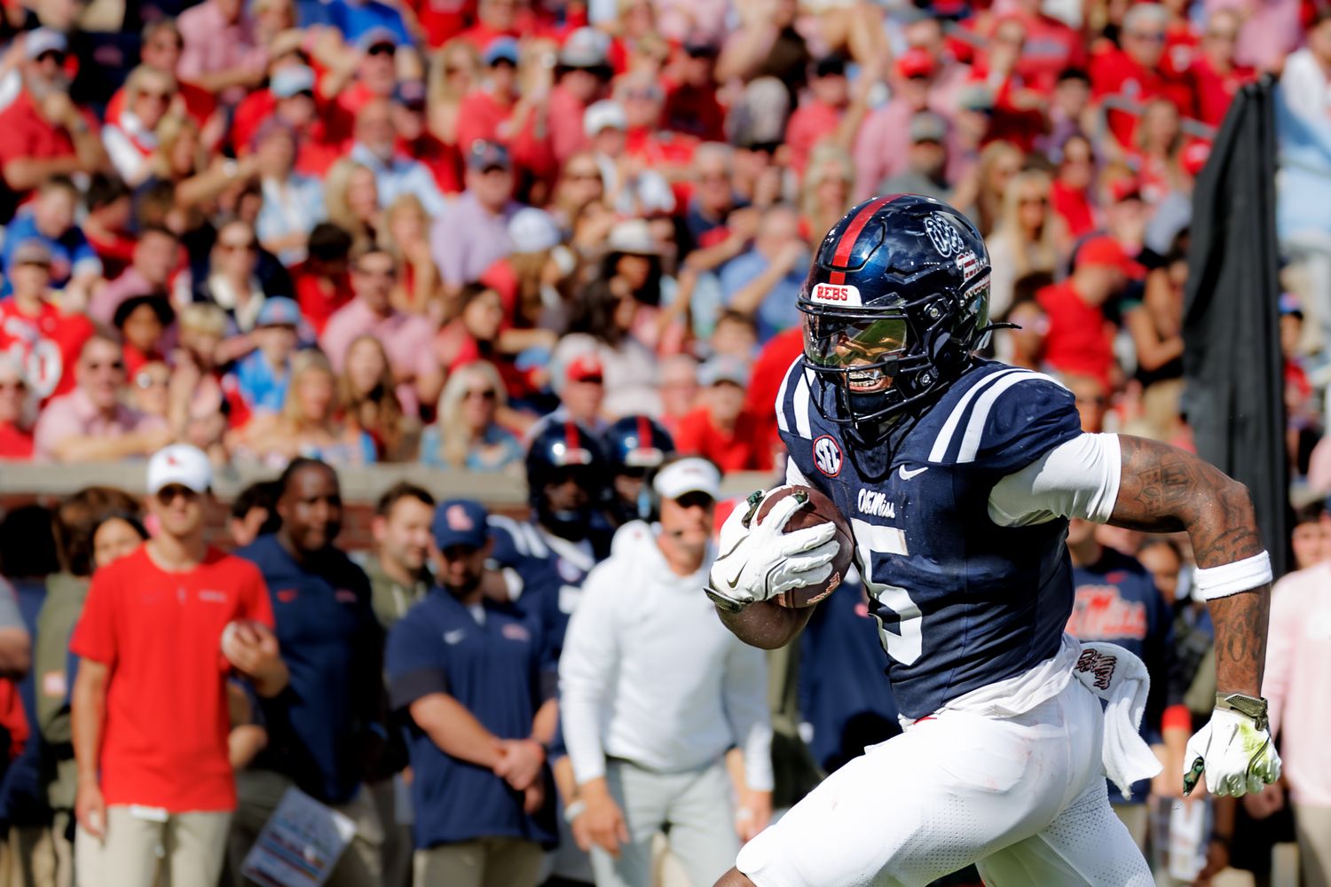 Ole Miss Rebels football player in navy uniform runs with ball during packed home game at Vaught-Hemingway Stadium.