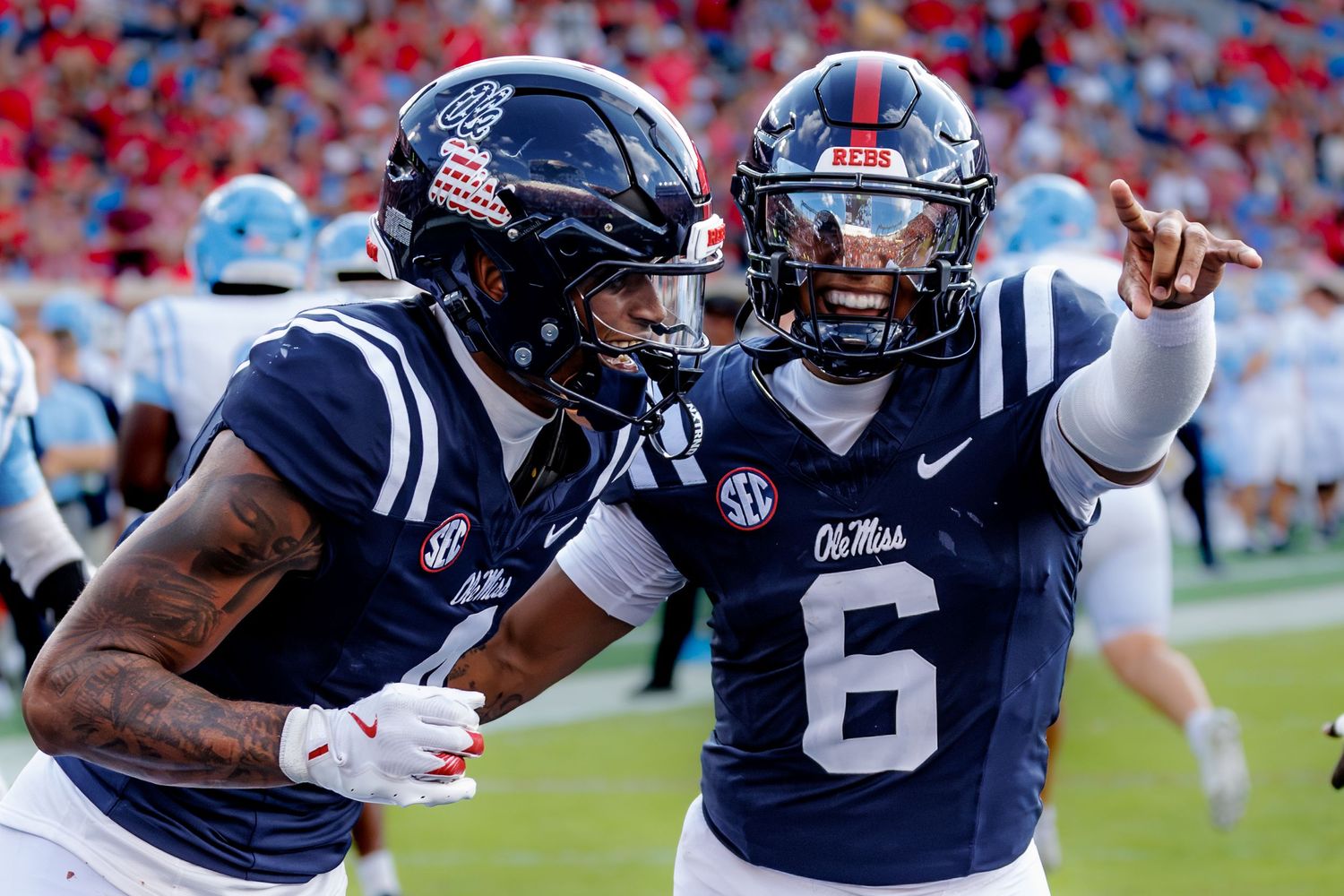 Two Ole Miss Rebels football players in navy uniforms celebrate on the field, with #6 pointing during a game.
