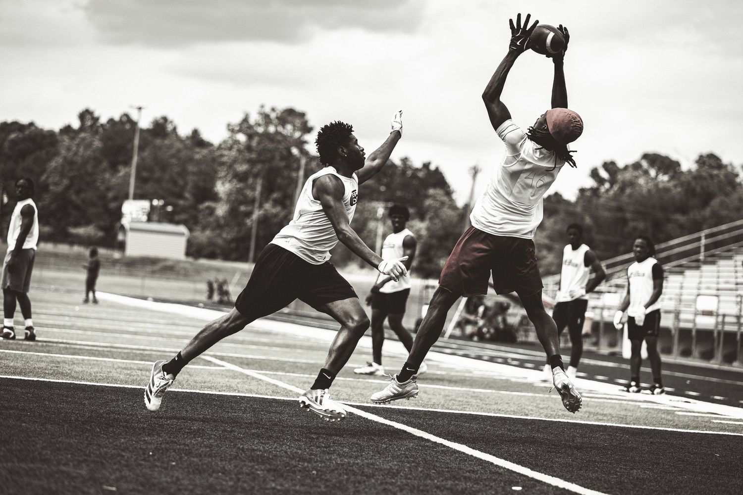 Two athletes compete for a football catch on a track field in a dynamic black and white action sports photo.