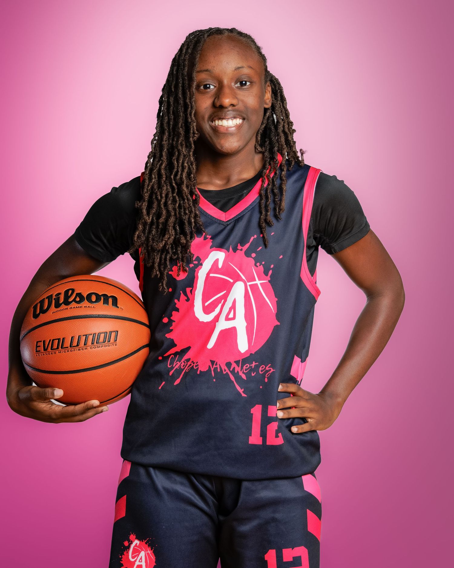 Young female basketball player in navy and pink CA jersey holding a Wilson Evolution ball against pink background.