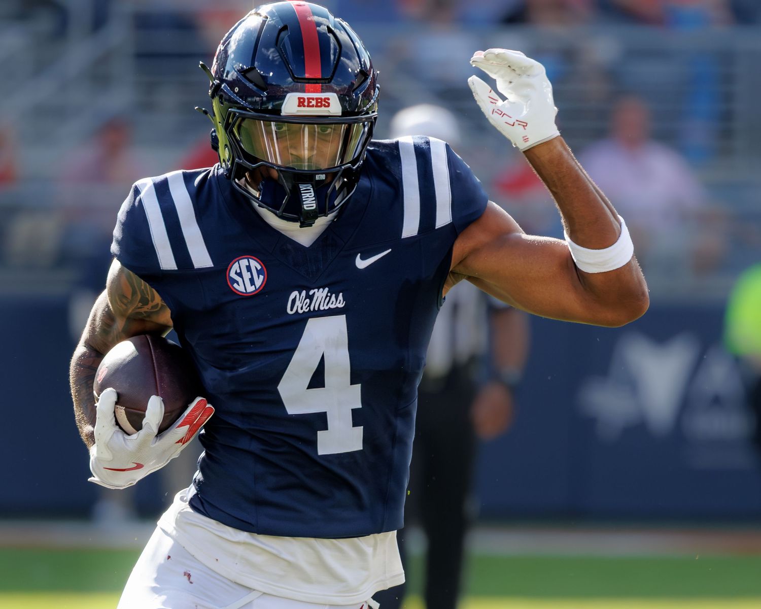 Ole Miss Rebels player #4 runs with football in navy SEC uniform during college football game.