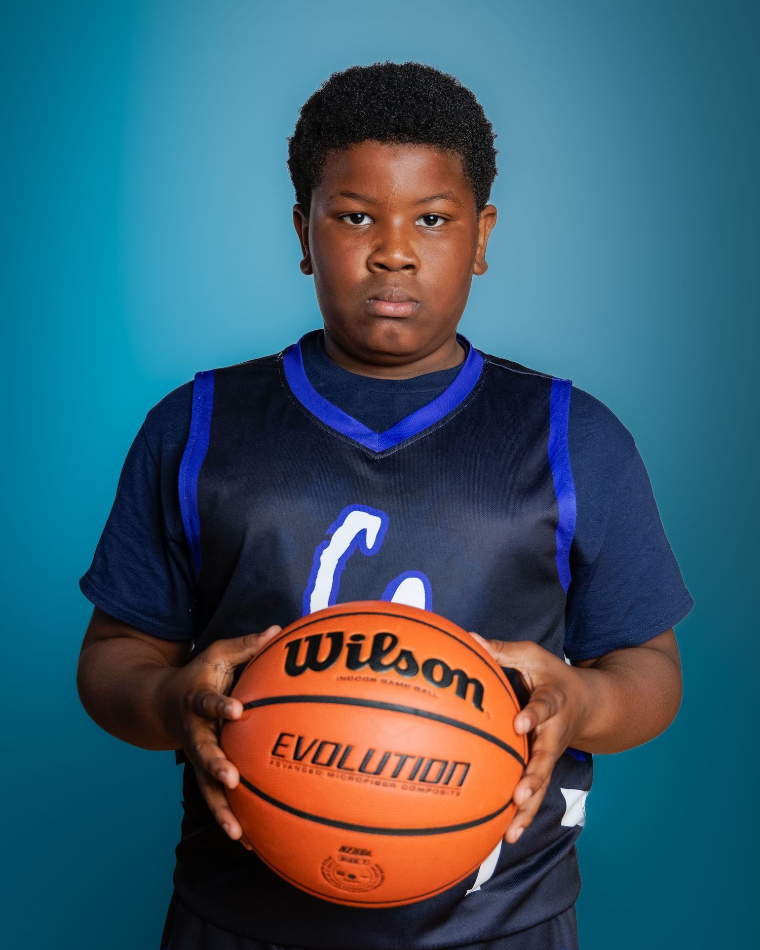 Young basketball player in navy blue jersey holding a Wilson Evolution basketball against a teal background.