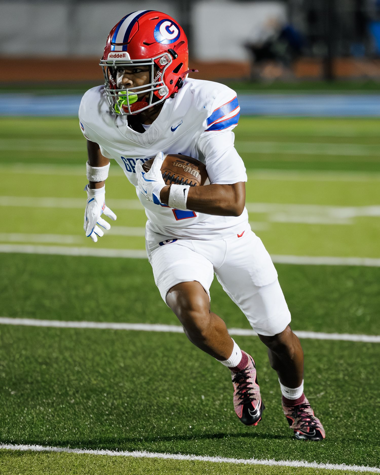 Georgia Bulldogs football player in white uniform carrying ball while running on field during game.