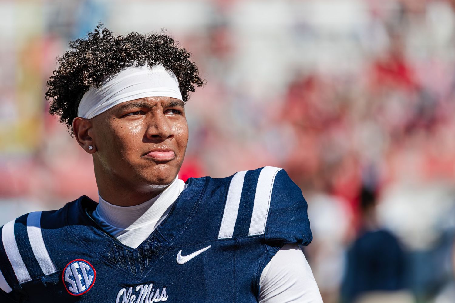 College football player in navy Ole Miss uniform with white headband looks to the side during a sunny game day.