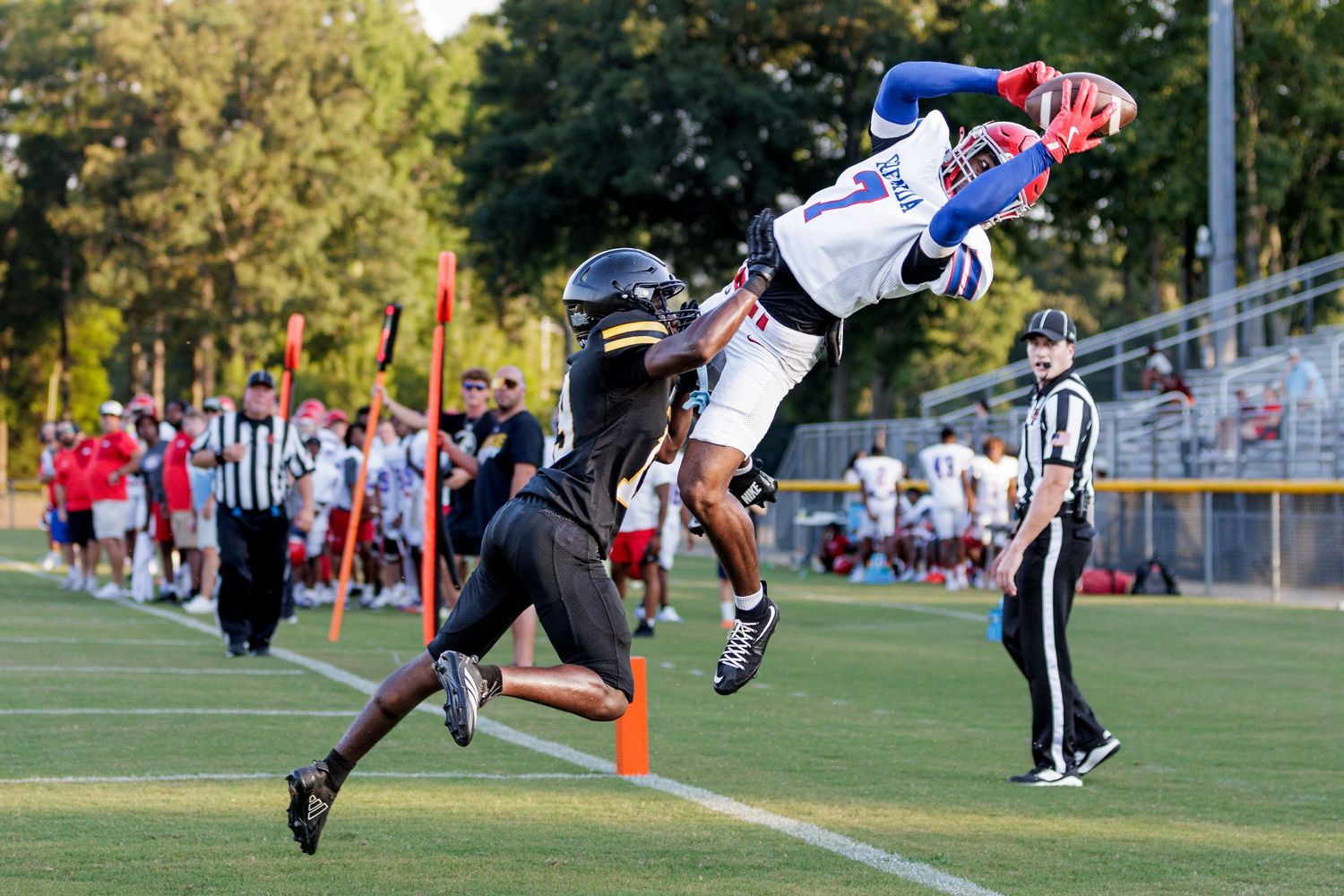Football player leaps high to catch a pass during a competitive high school football game under clear skies.
