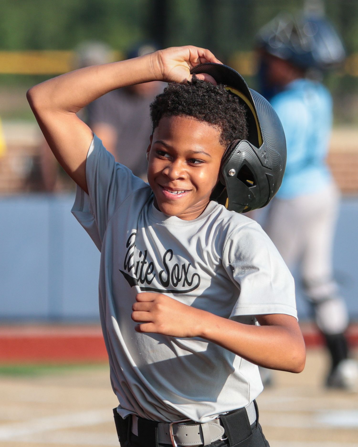 Young baseball player adjusts batting helmet with a bright smile during a game.