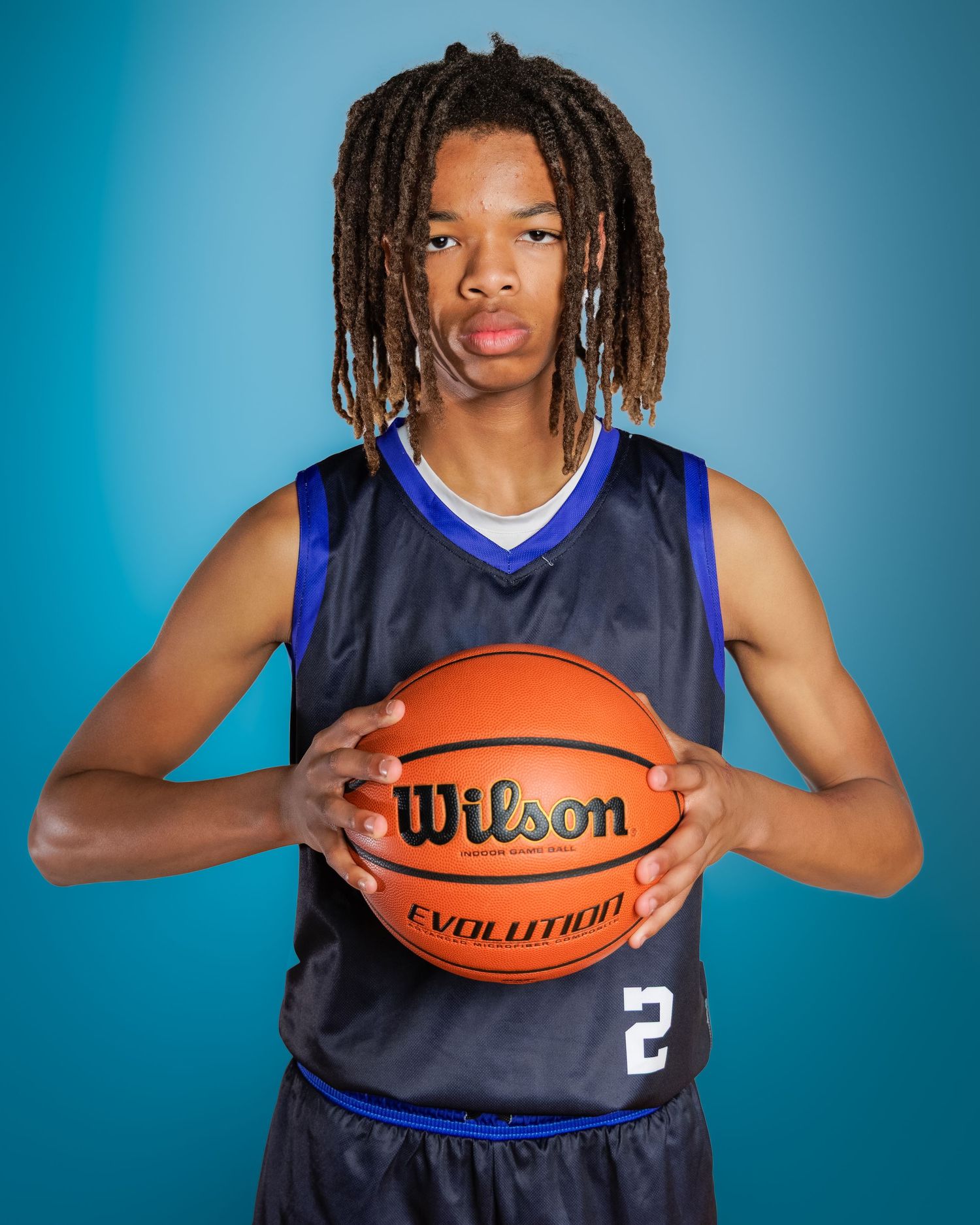 Young basketball player wearing #2 jersey holds a Wilson Evolution basketball against a blue background.