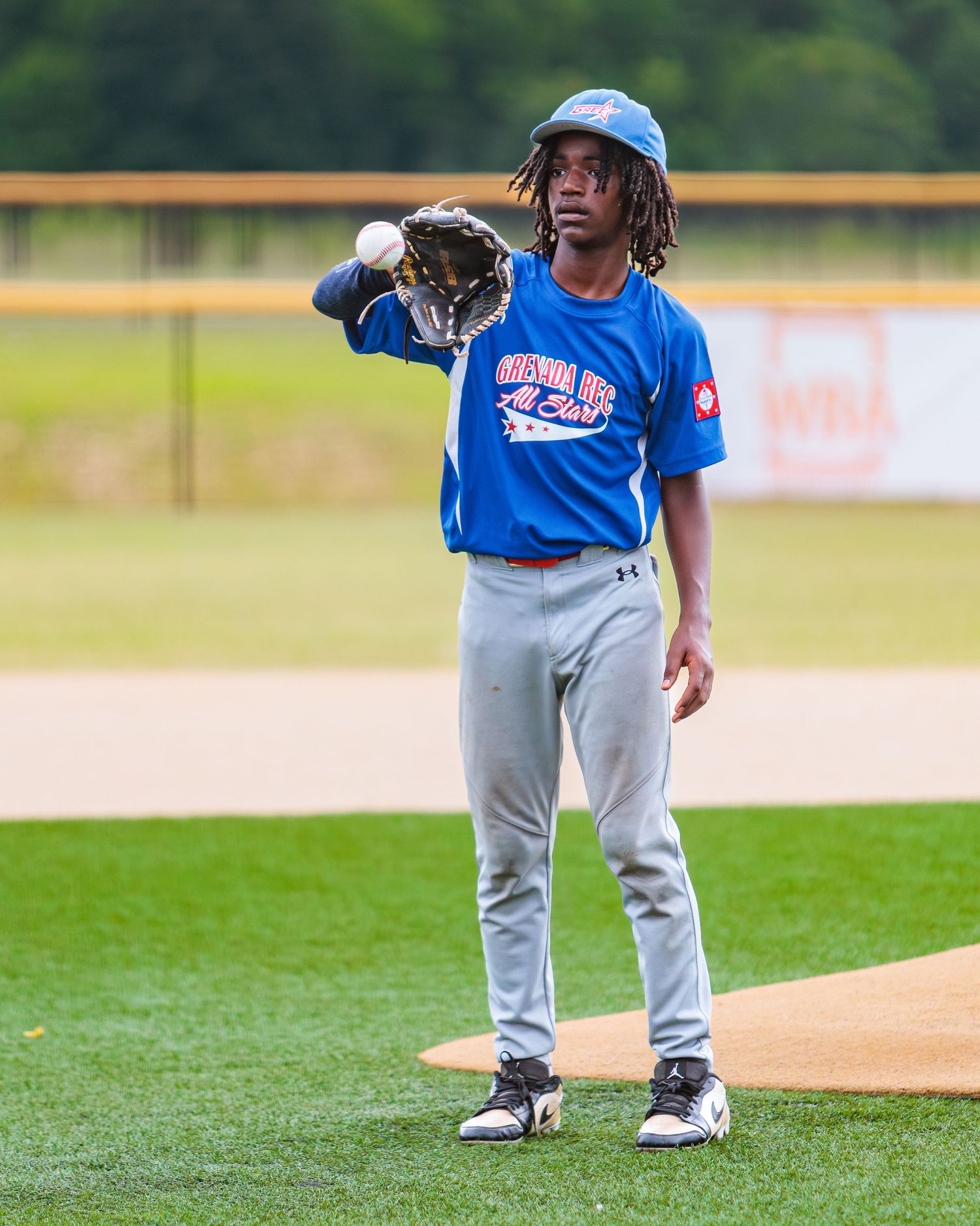Baseball player in blue uniform stands on pitcher's mound with glove during game.