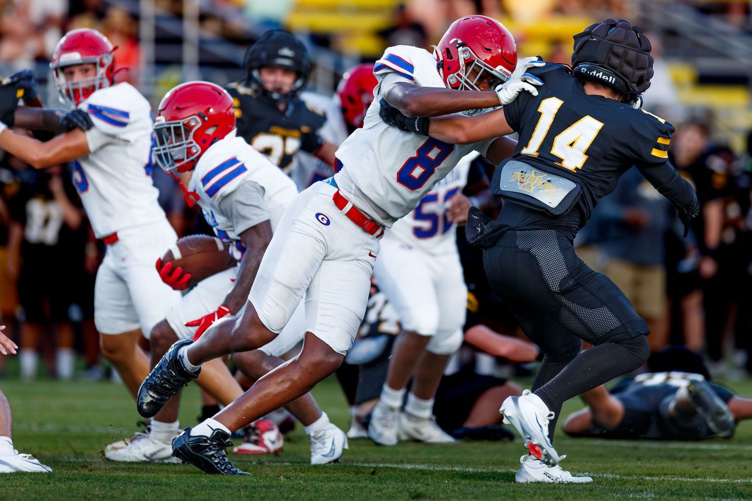 High school football players in red and white uniforms compete against a team in black during an intense game play.