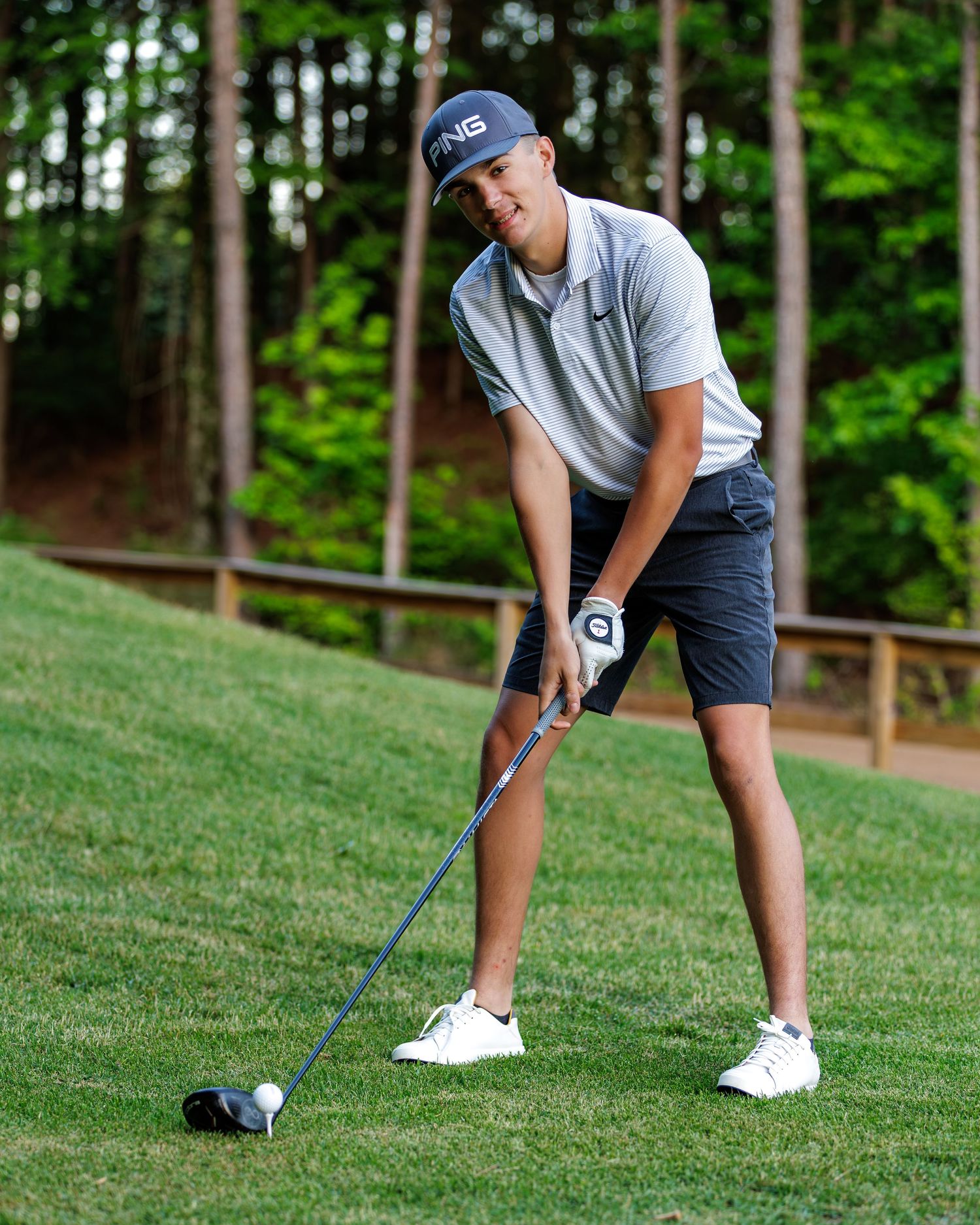 Young golfer in PING cap and Nike polo prepares to swing a club on a lush green golf course.
