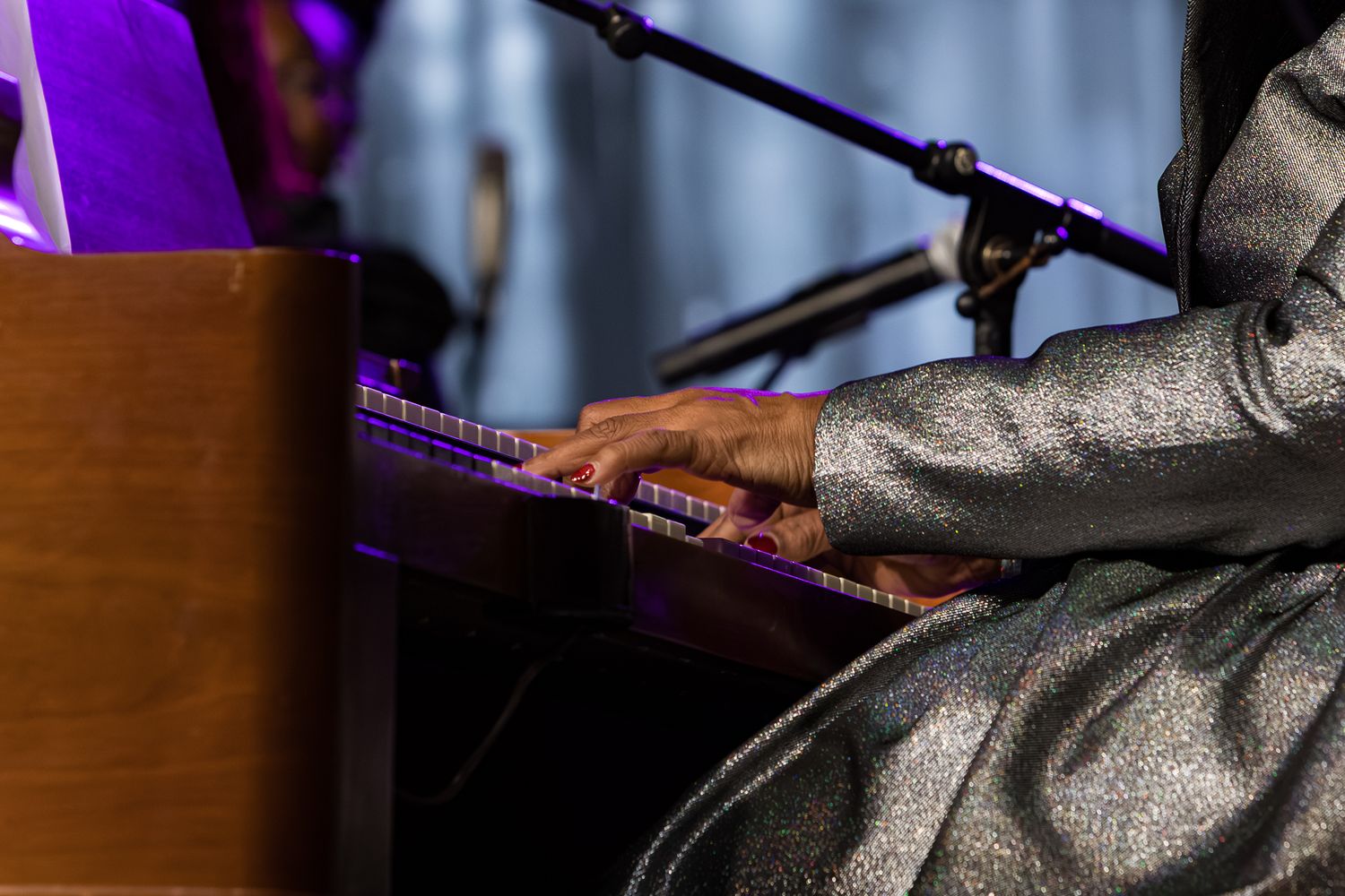 A musician performs on a keyboard while wearing a sparkly silver outfit in a dimly lit venue.