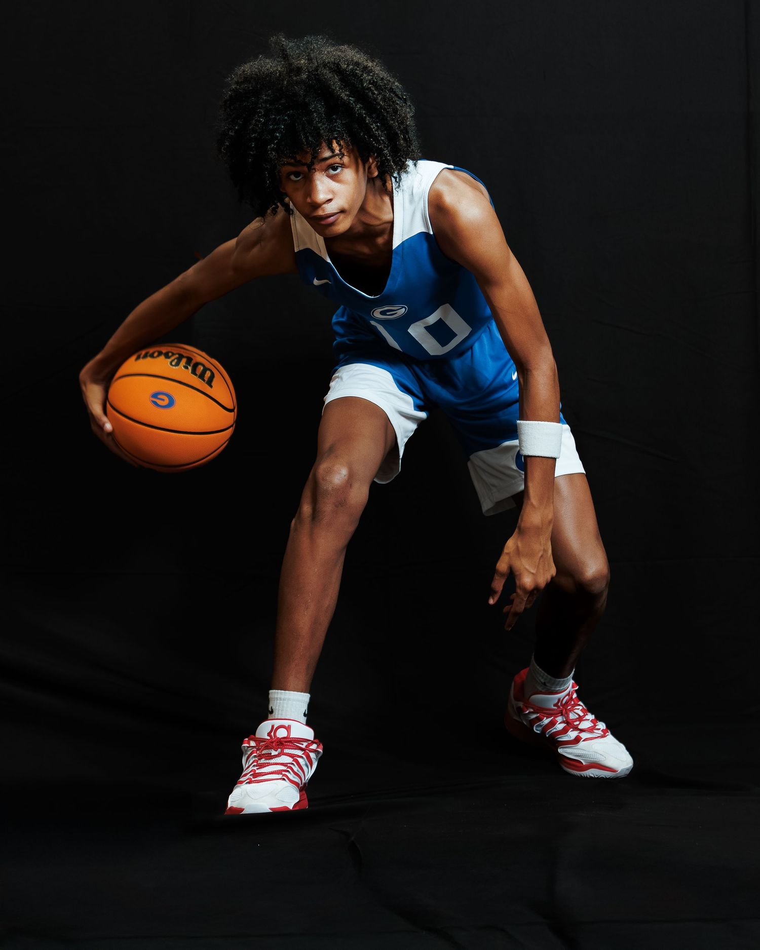 Young basketball player in blue jersey dribbles a Spalding ball, posing dynamically against a dark studio background.