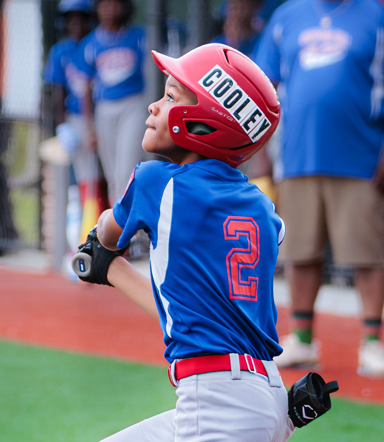 Youth baseball player in red helmet and blue jersey watches the field during a game.