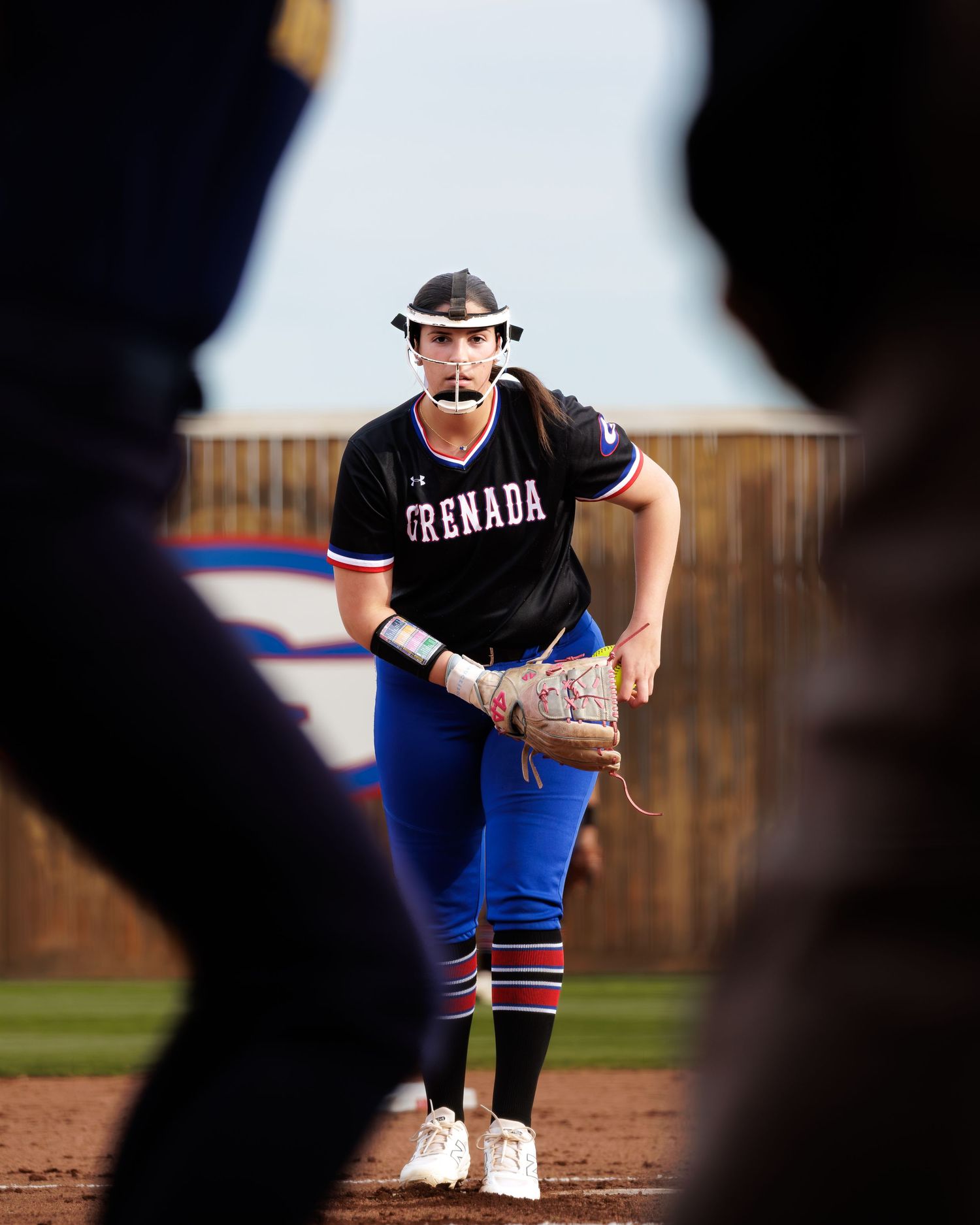 A softball player in a Grenada uniform stands ready in position on the field during a game.