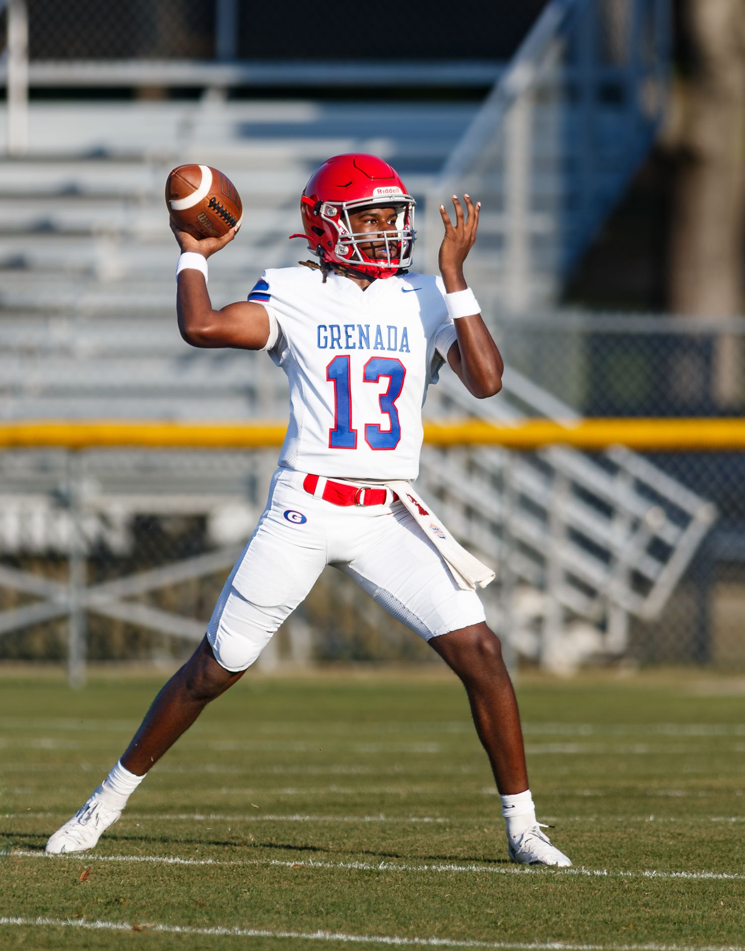 Grenada #13 quarterback in white uniform prepares to throw a pass during a high school football game.