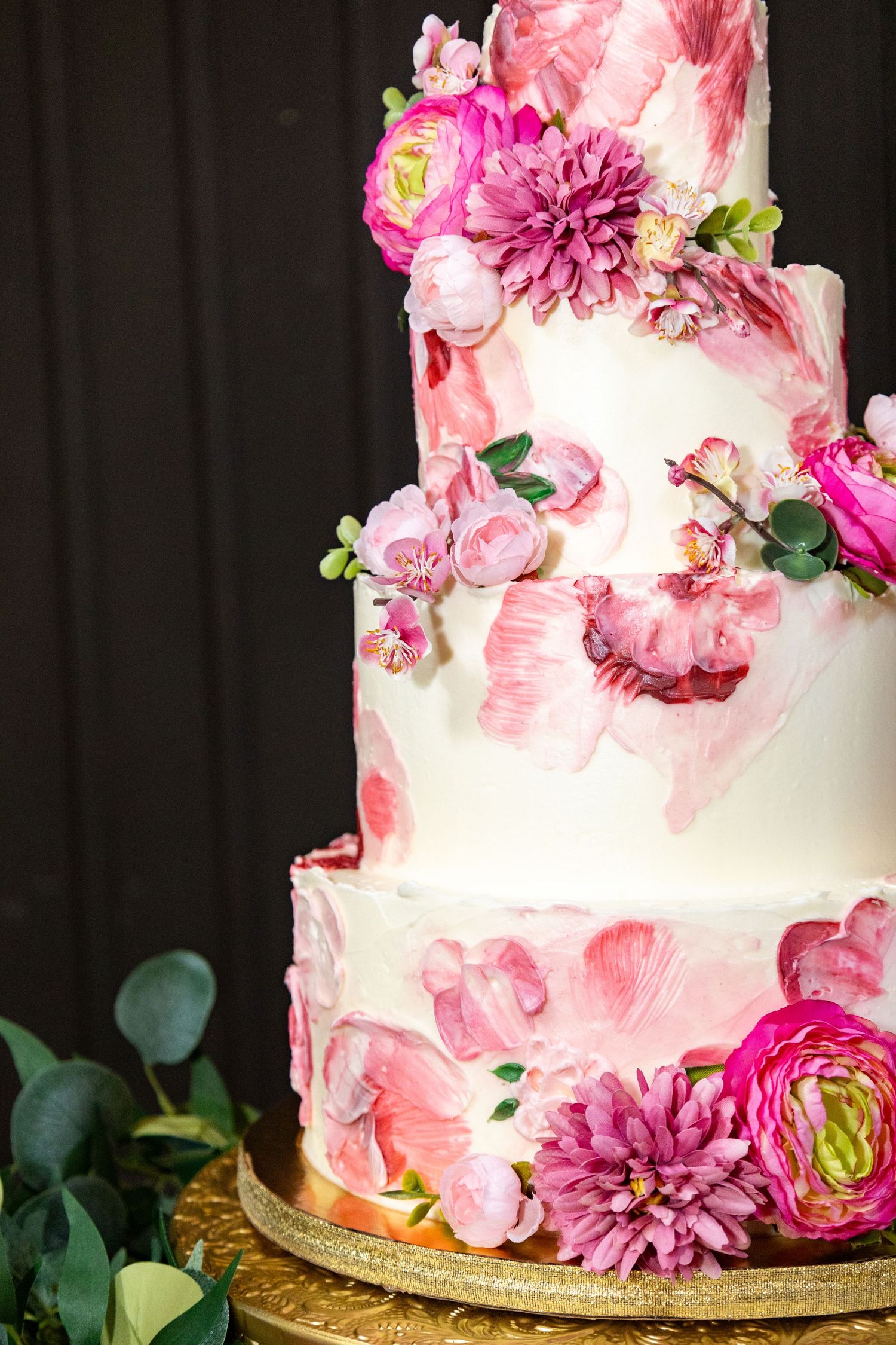 An elegant wedding cake decorated with pink dahlias and roses against a dark background.