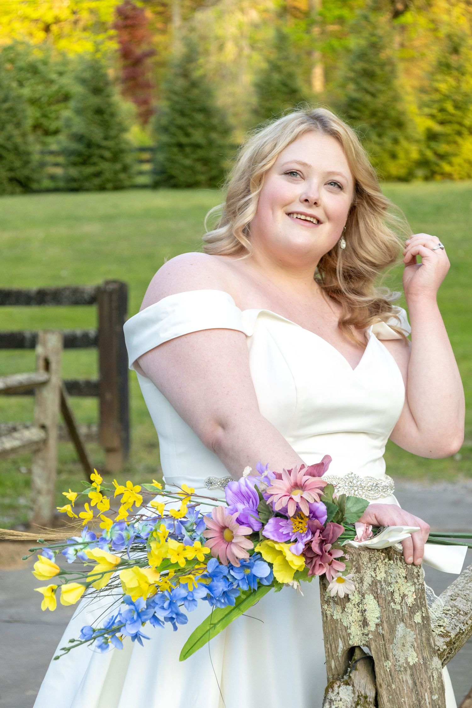 A bride in an off-shoulder gown poses with colorful spring flowers in a garden setting.