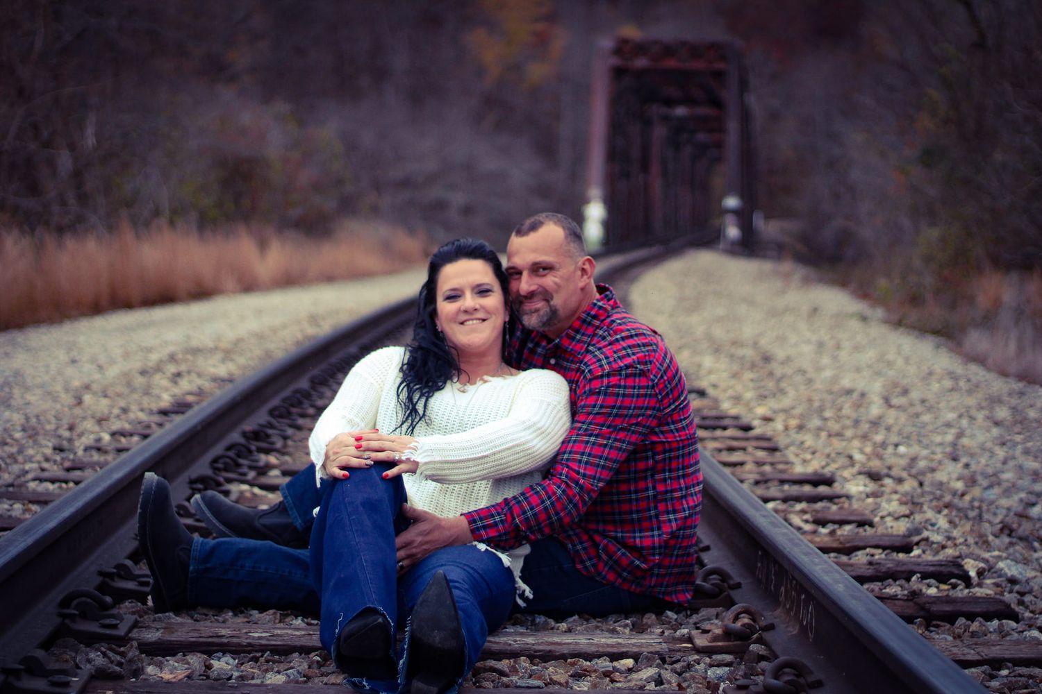 A couple sits together on railroad tracks for an intimate photo session.