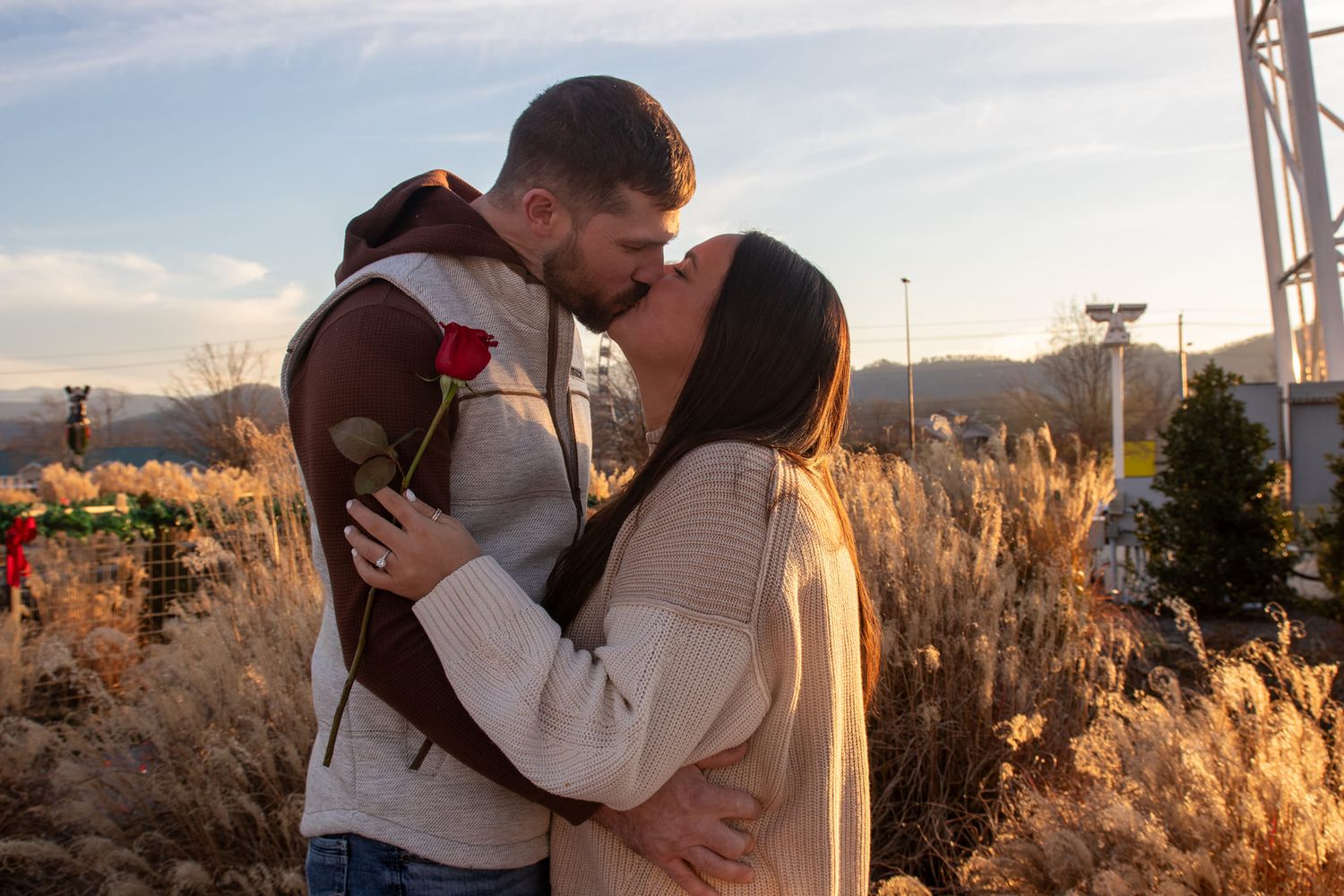 A couple shares a romantic kiss amid golden winter grass at sunset.