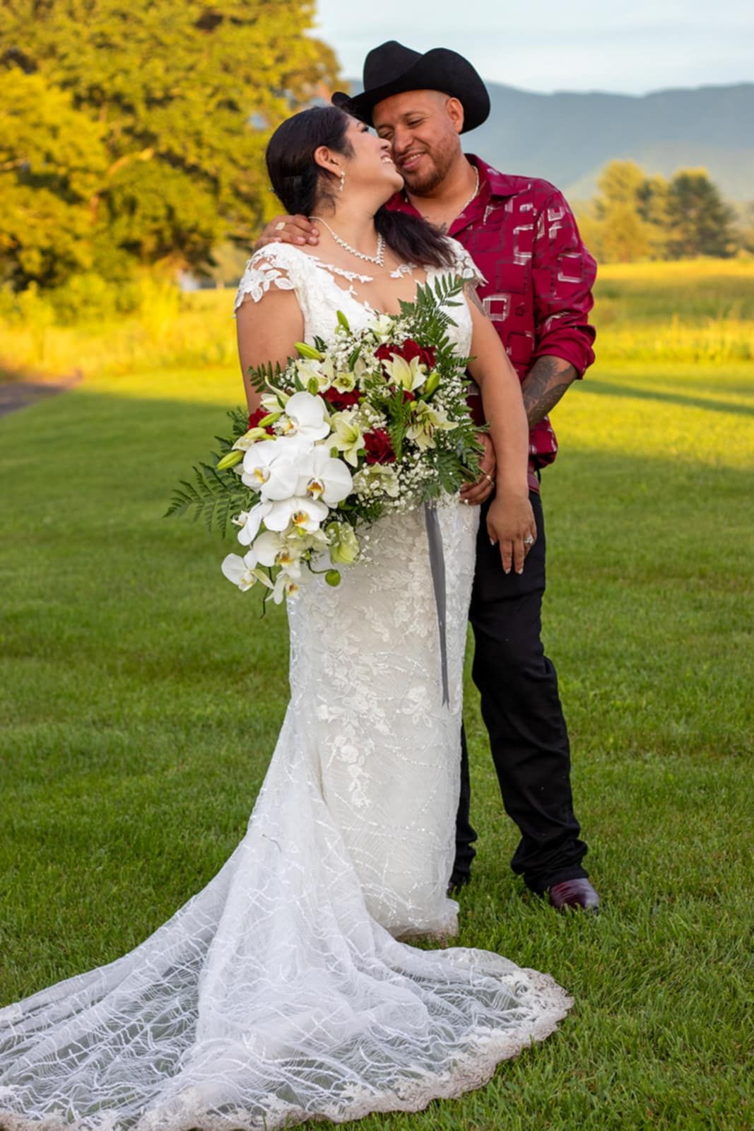 A couple shares a joyful moment against yellow wildflowers, with the bride holding a lush white and burgundy bouquet.