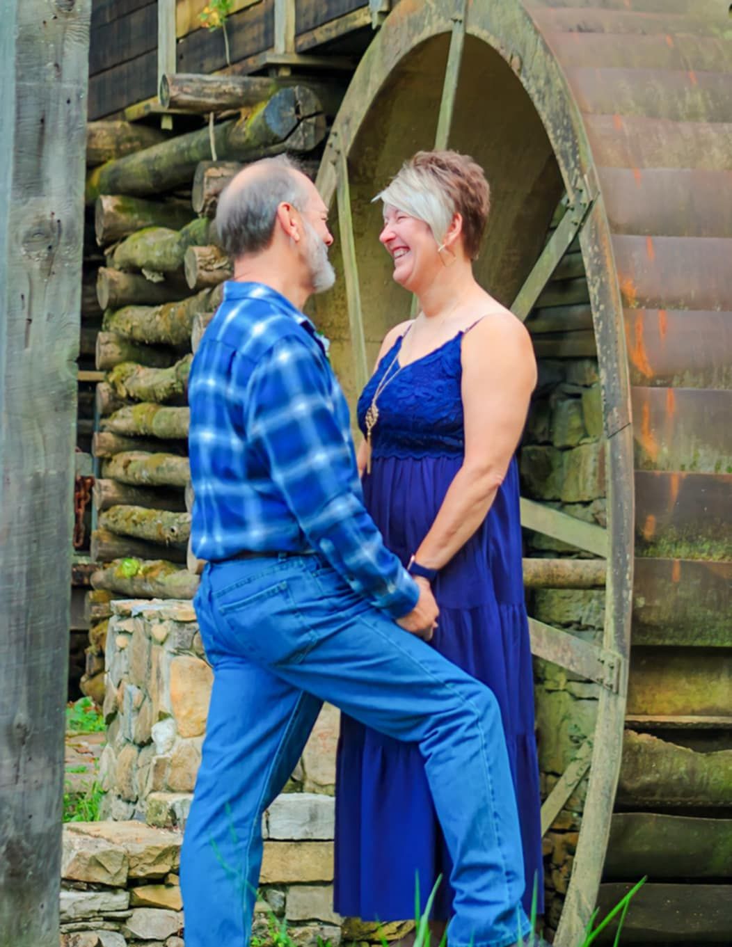A couple shares a romantic moment by an old wooden water wheel.