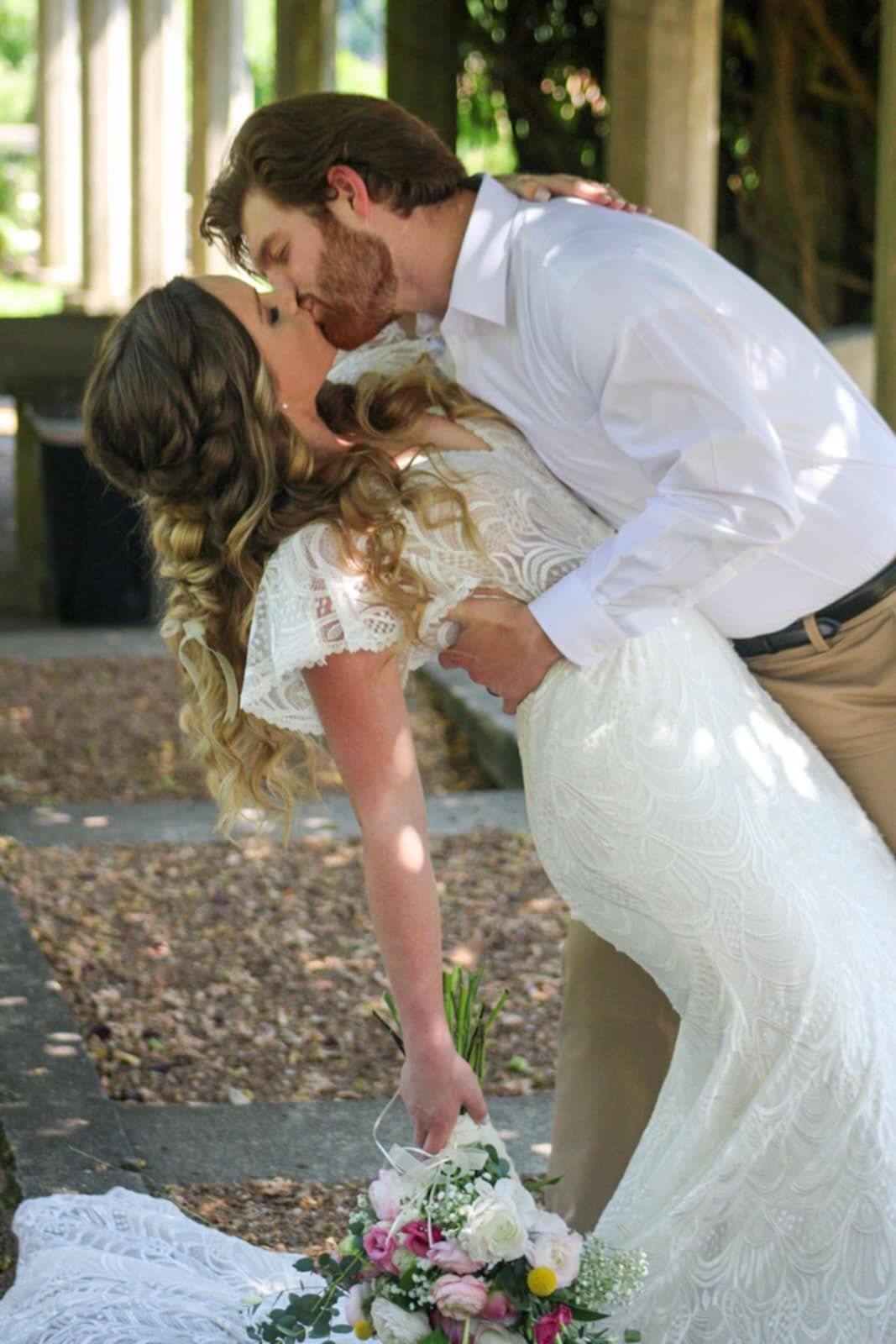 A romantic dip kiss captured in a garden setting with scattered sunlight.