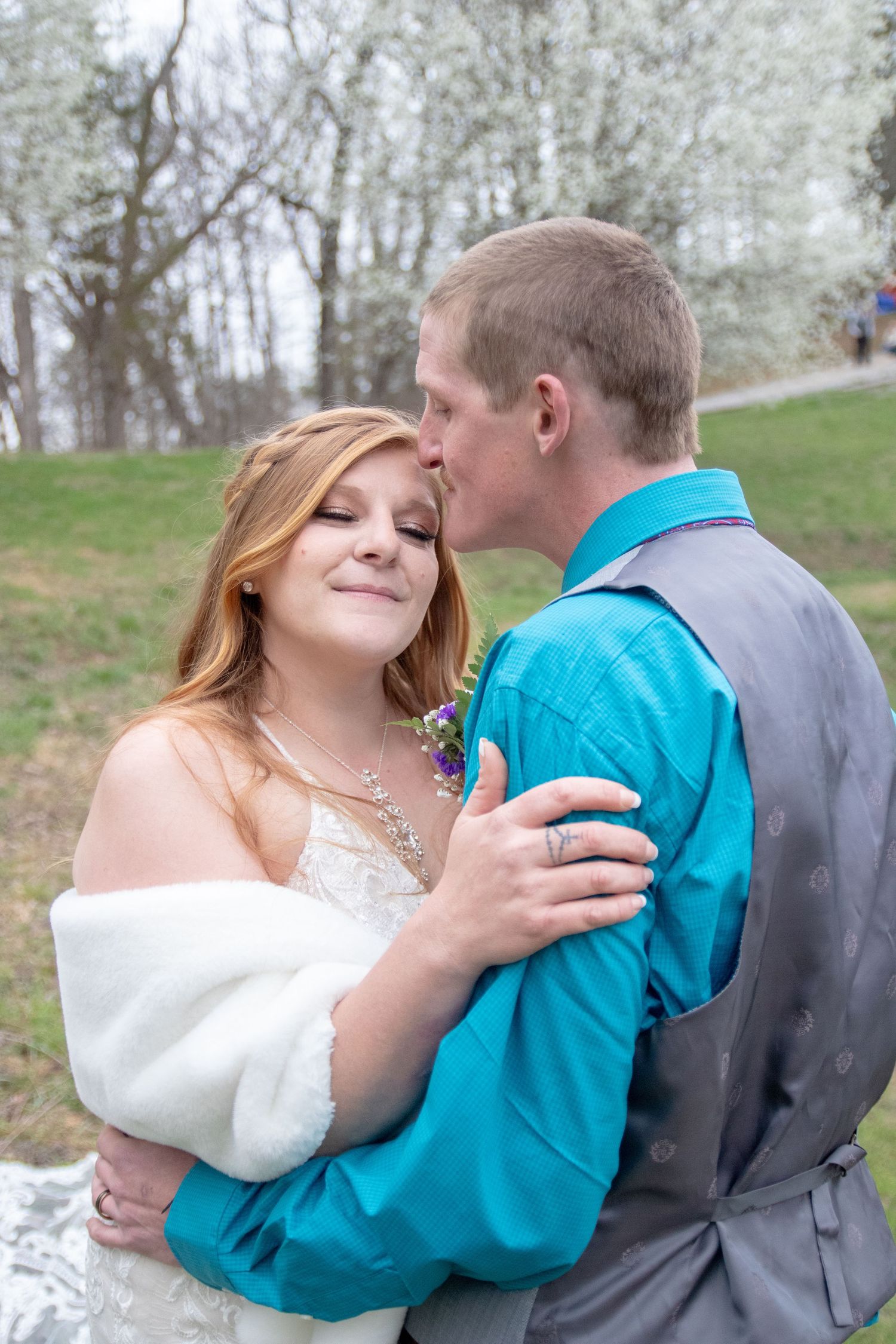 A romantic couple shares a tender moment outdoors in spring, with the bride wearing a white dress and shawl.