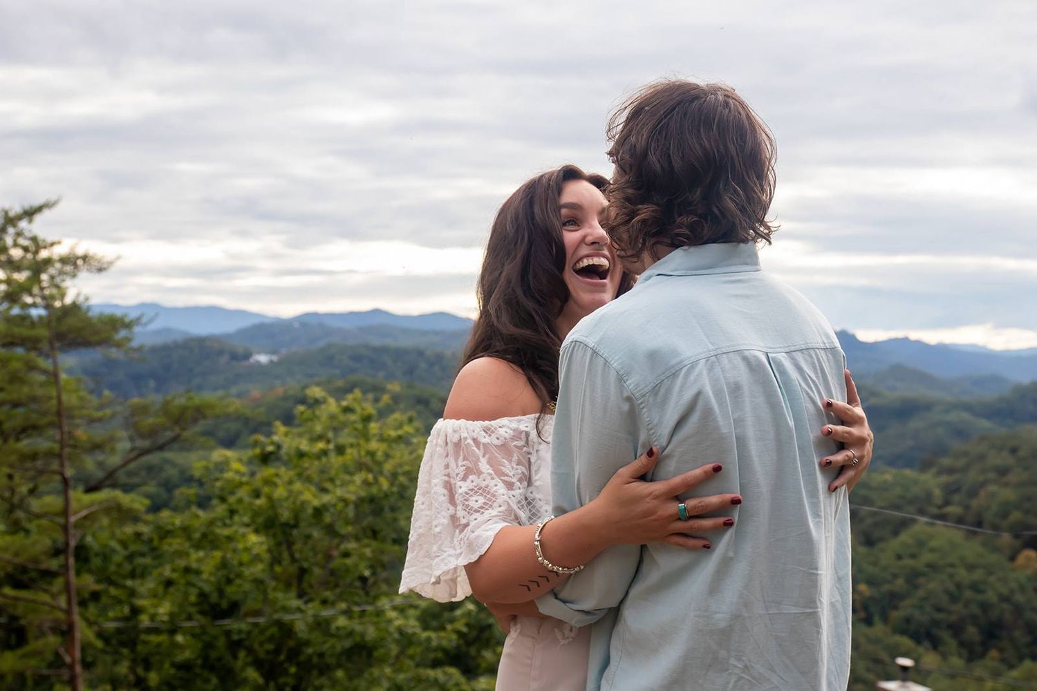 Couple embracing and laughing together on mountain overlook with scenic valley view.